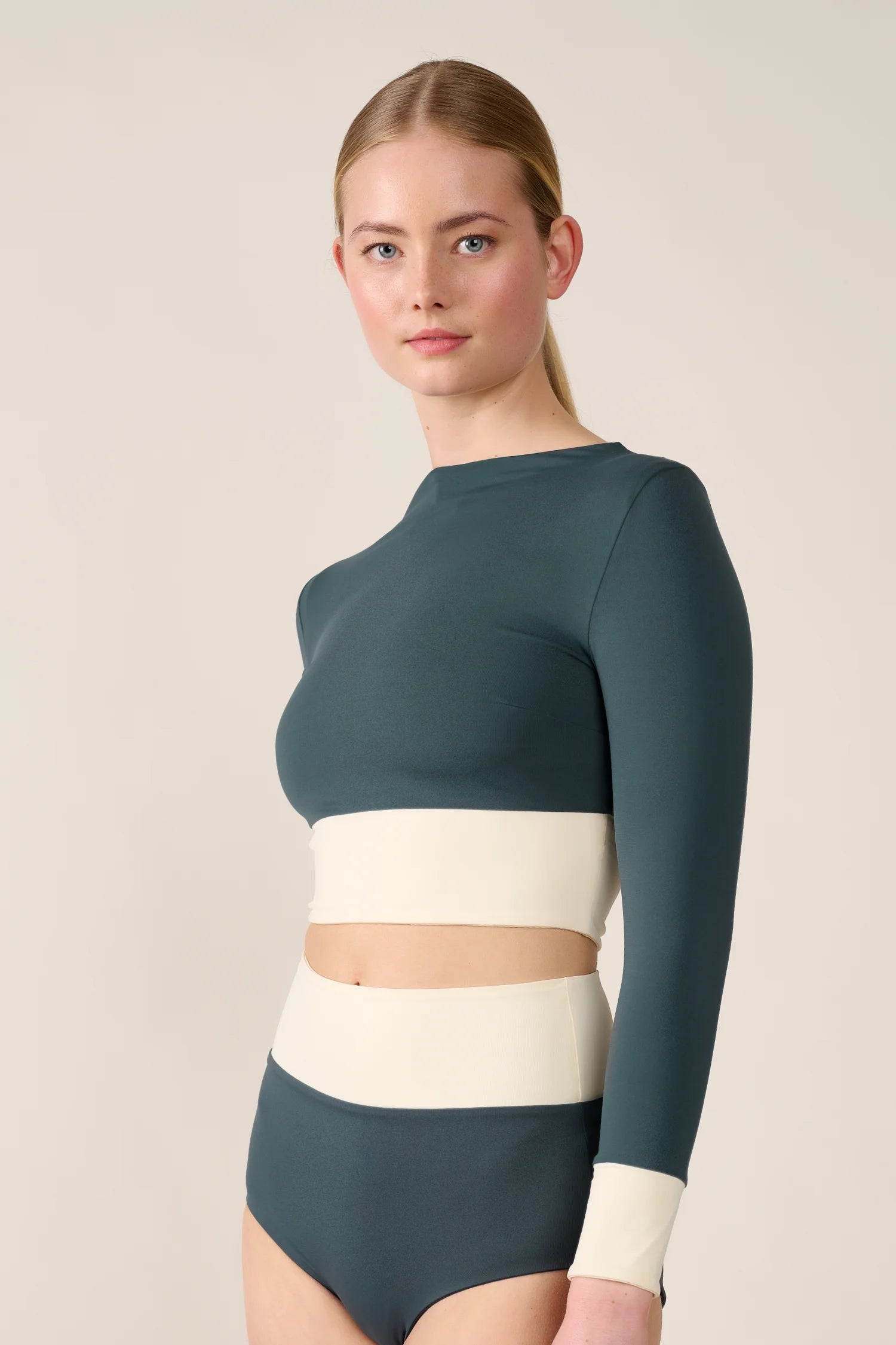 Frau trägt MYMARINI Badeanzug mit langen Ärmeln, hoch geschlossen, in Dunkelgrün und Creme.#color_black-grey-white