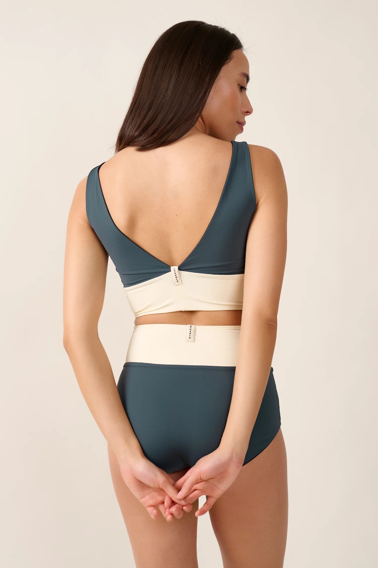 Frau trägt MYMARINI Bikinitop mit V-Ausschnitt und Bikinihose in High Waist. Rückenansicht, schlichtes Design.#color_black-grey-white