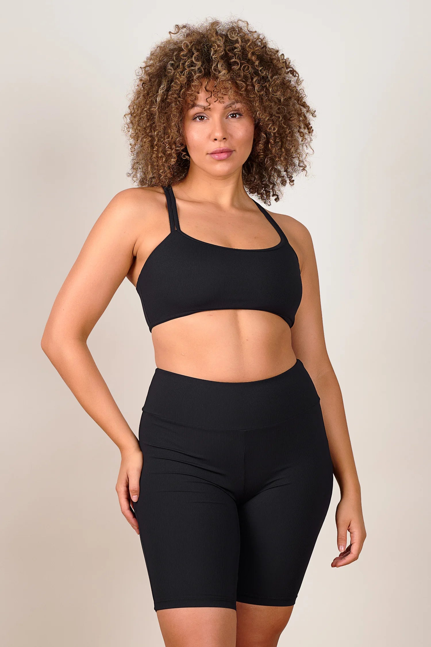 Frau trägt MYMARINI Bikinitop mit breiten Trägern und High-Waist-Bikinihose in Schwarz, stehend vor neutralem Hintergrund.#color_black