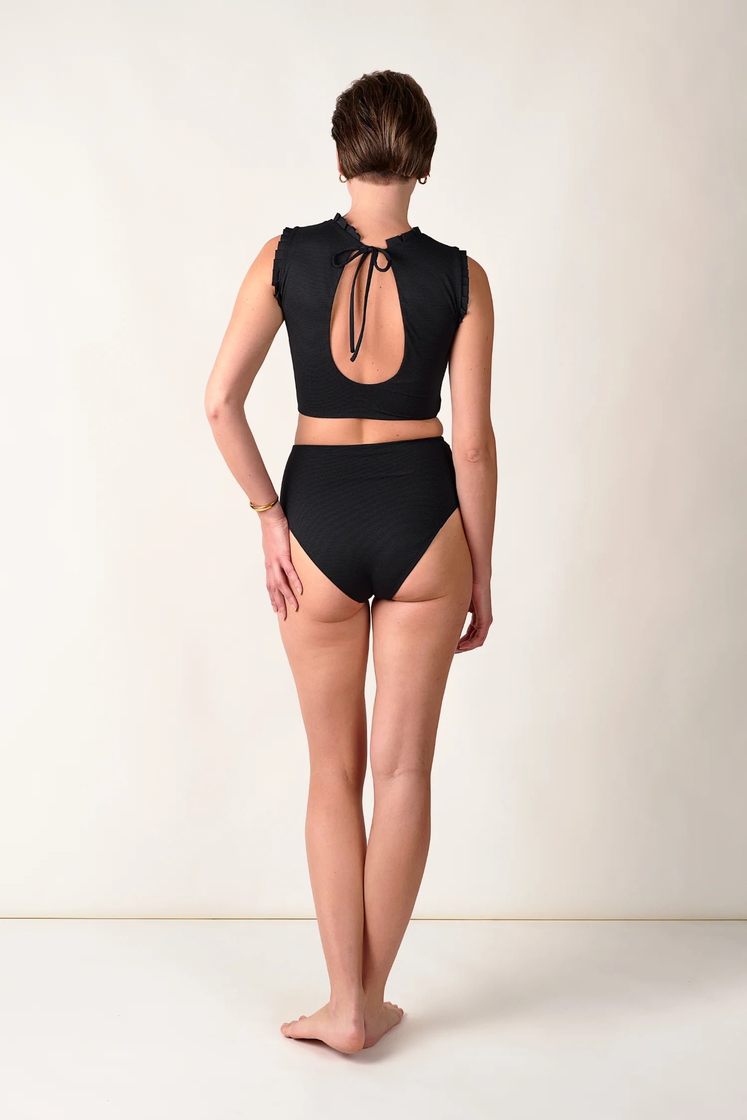 Rückansicht einer Frau in schwarzem MYMARINI-Bikinitop mit tiefem Rückenausschnitt und passender High-Waist-Bikinihose.#color_black