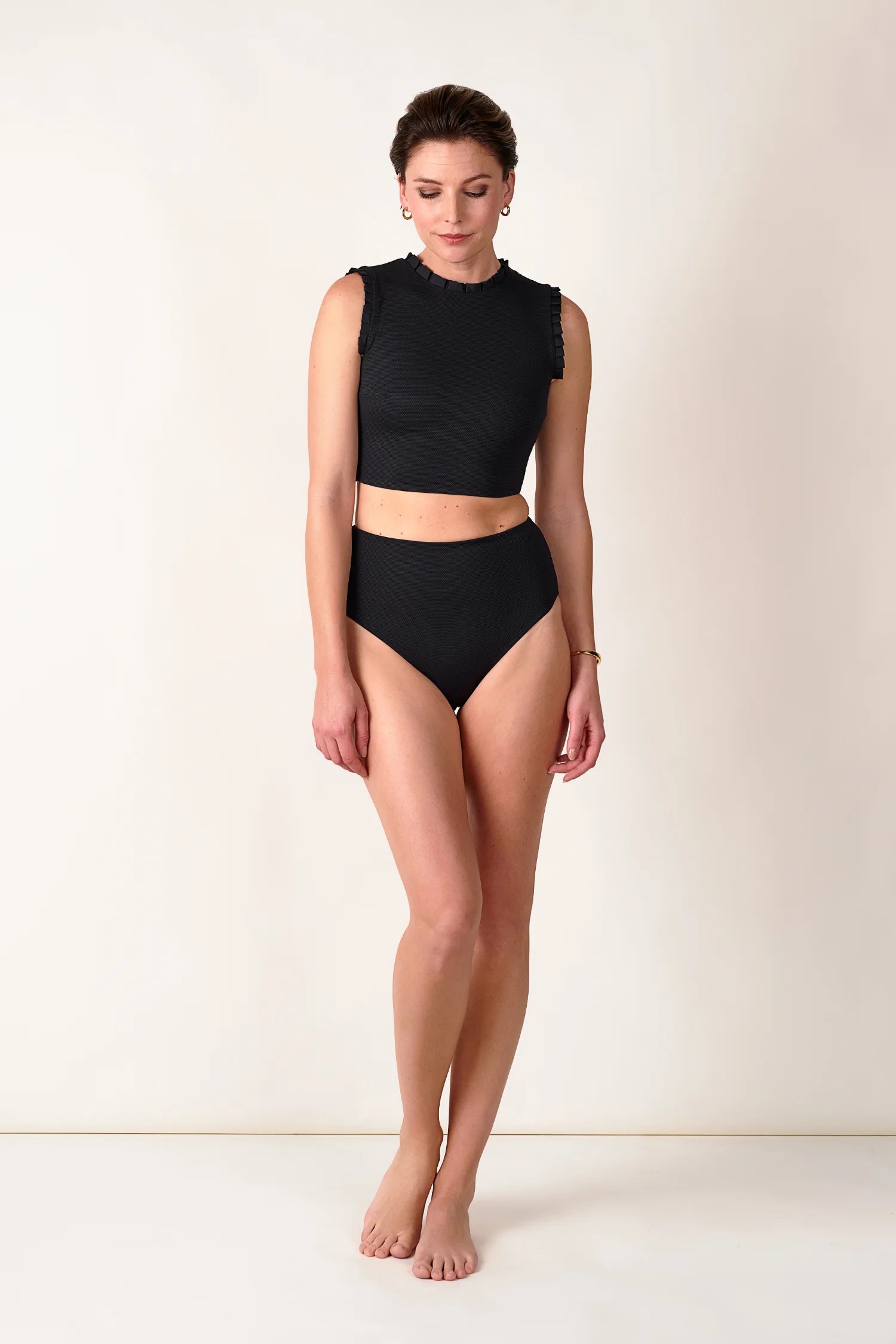 Frau trägt schwarzen MYMARINI Bikini mit hochgeschlossenem Top und hoch geschnittener Bikinihose vor neutralem Hintergrund.#color_black