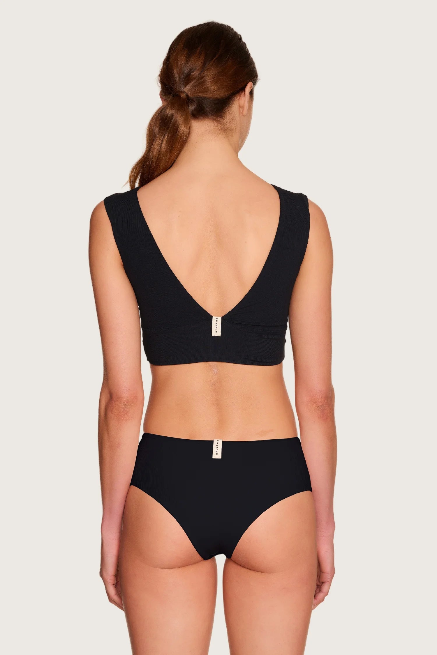 Rückansicht einer Person in schwarzem MYMARINI-Bikinitop mit V-Ausschnitt und passender Bikinihose, mid rise.#color_black