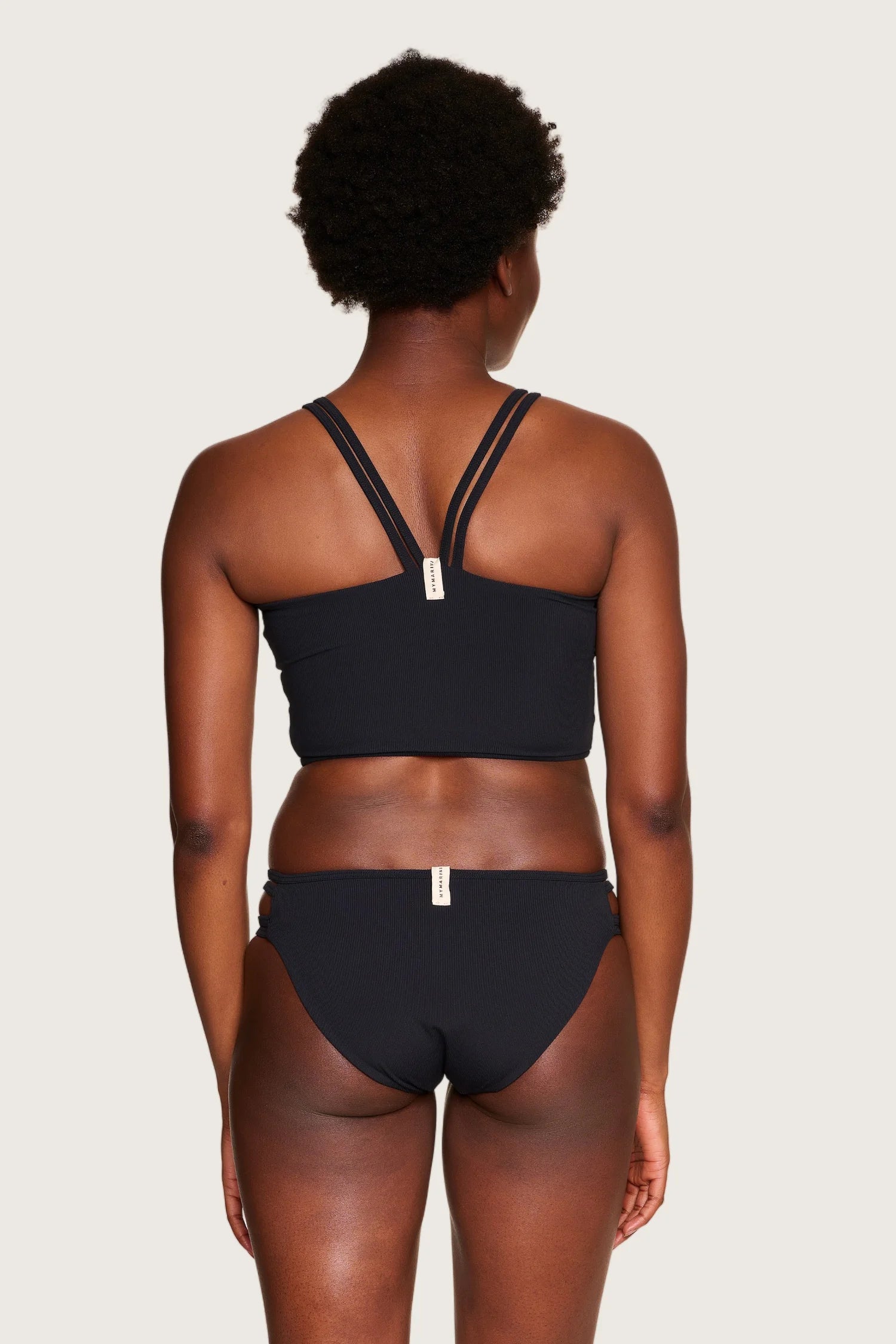 Rückansicht einer Person in schwarzem MYMARINI-Bikini mit breiten Trägern und hohem Beinausschnitt.#color_black