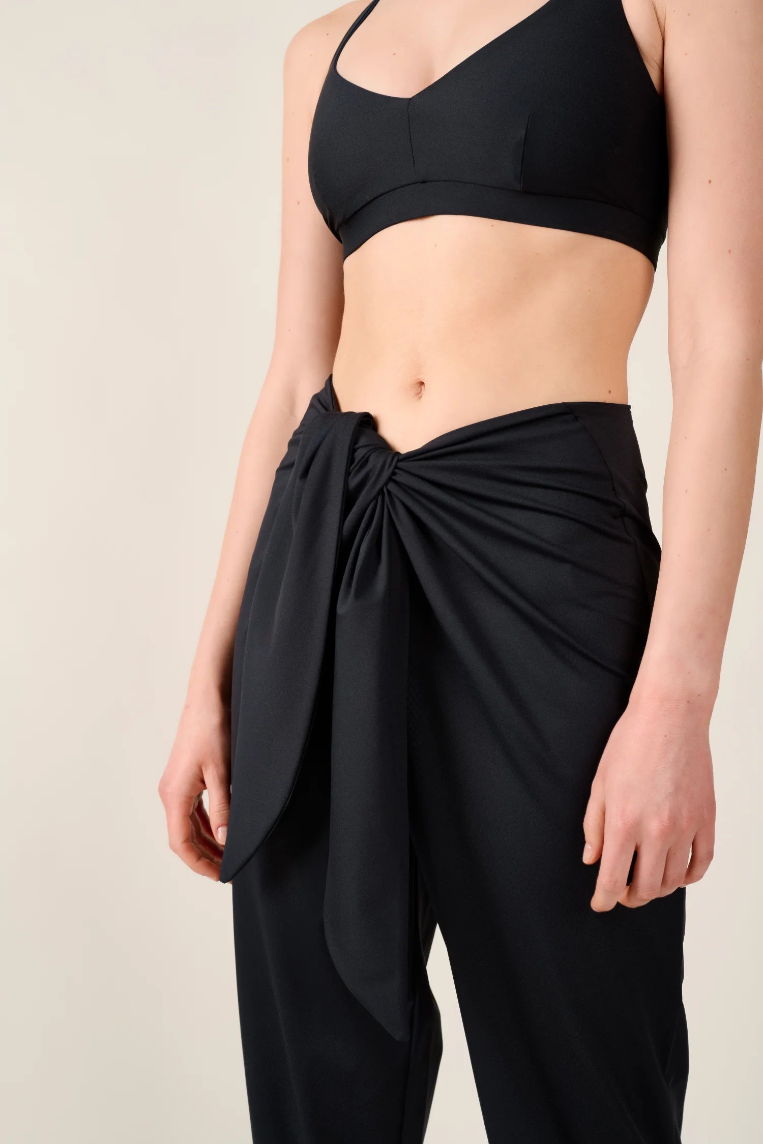 Frau trägt schwarzes MYMARINI-Bikinitop mit Spaghettiträgern und schwarze Hose mit Knoten vorne.#color_black