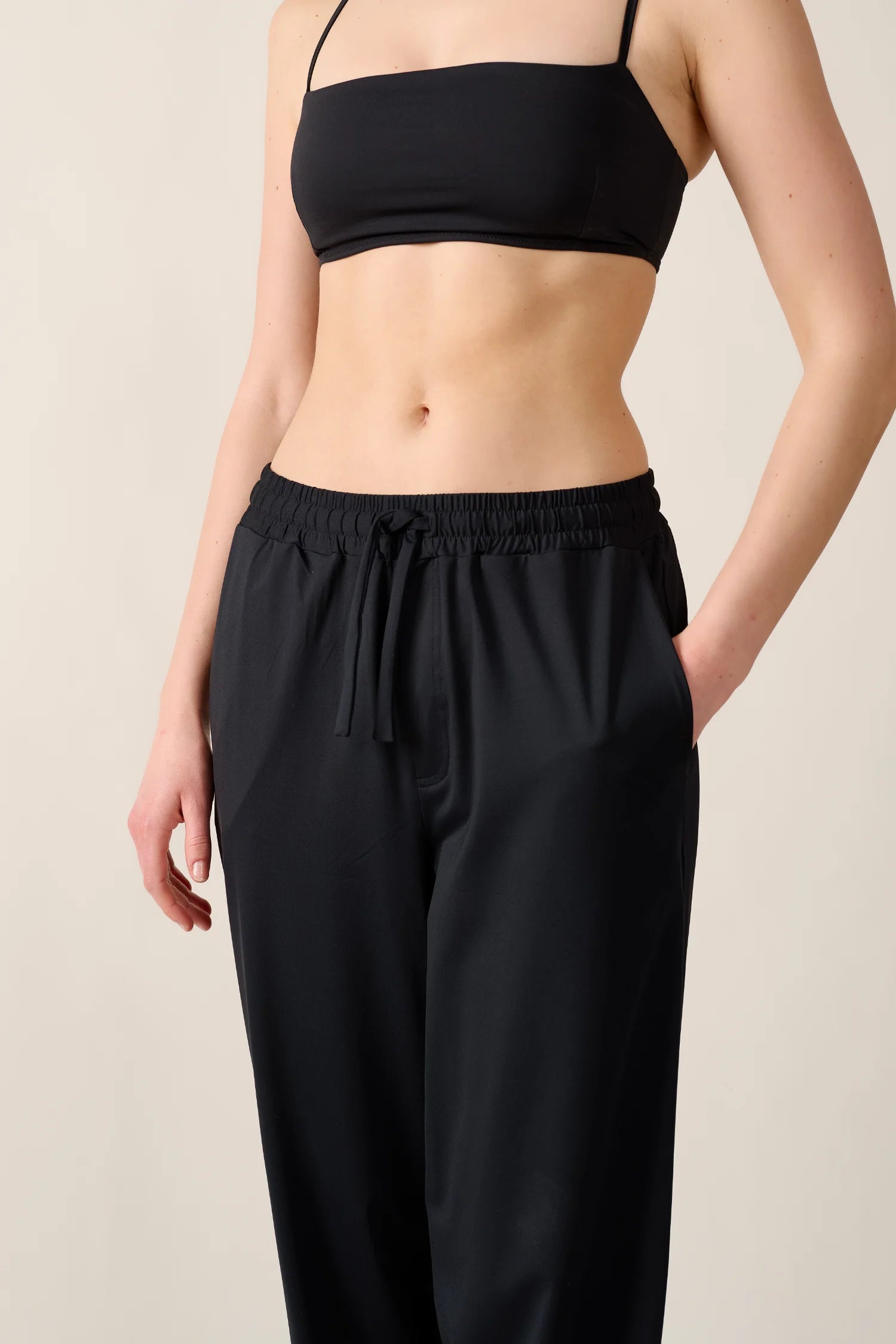 Frau trägt MYMARINI Bikinitop mit Spaghettiträgern und schwarze Hose, stehend vor neutralem Hintergrund.#color_black