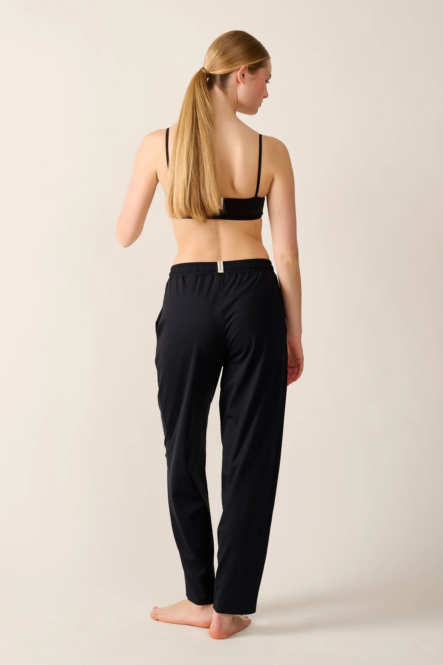 Frau in schwarzem MYMARINI Bikinitop mit Spaghettiträgern und schwarzer Hose, von hinten gesehen.#color_black