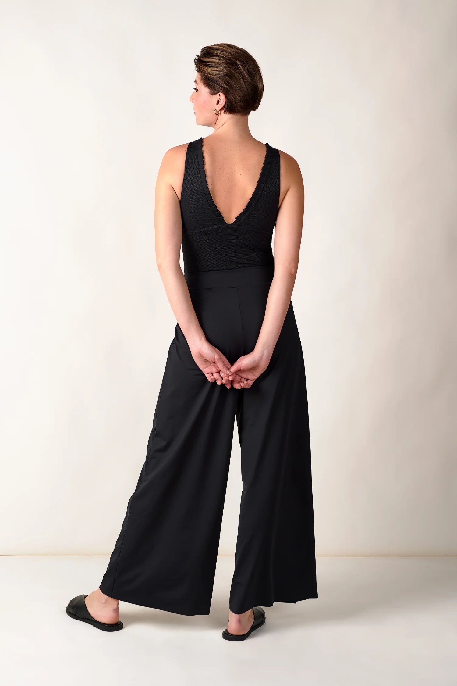 Frau in schwarzem MYMARINI V-Ausschnitt-Top und weiter Hose, von hinten.#color_black