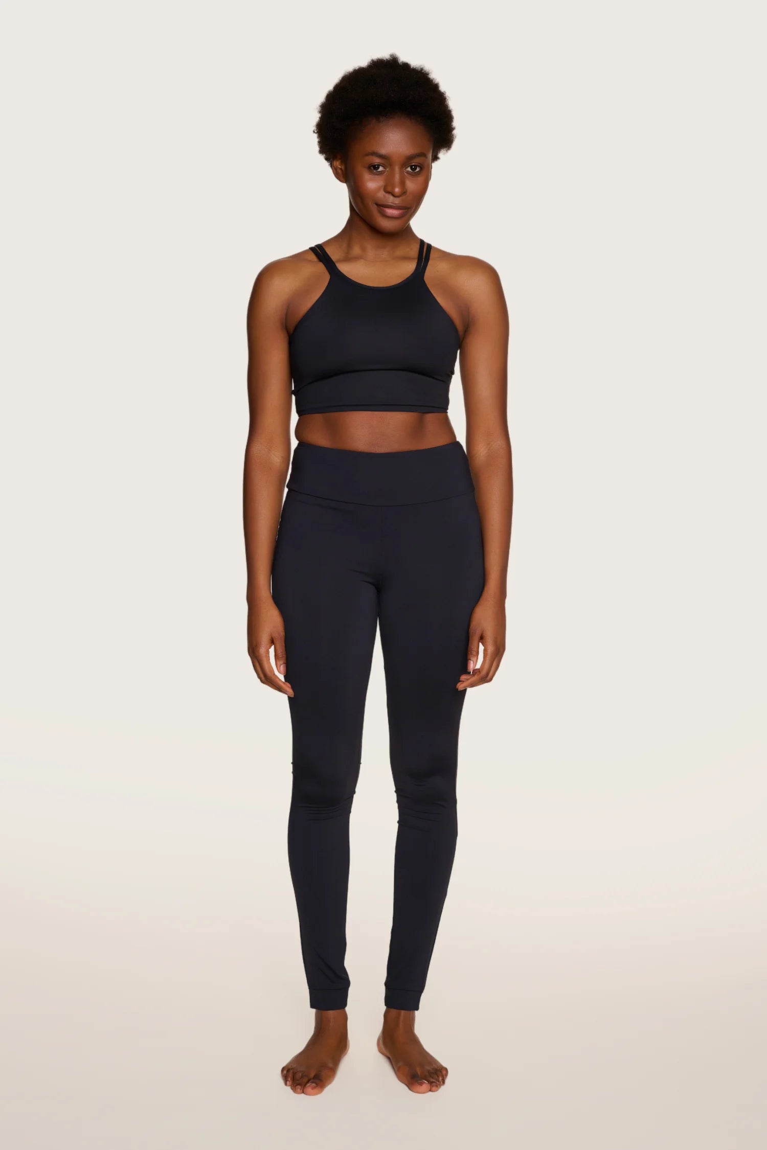 Frau trägt MYMARINI Top mit Spaghettiträgern und Leggings in Schwarz, stehend vor hellem Hintergrund.#color_black