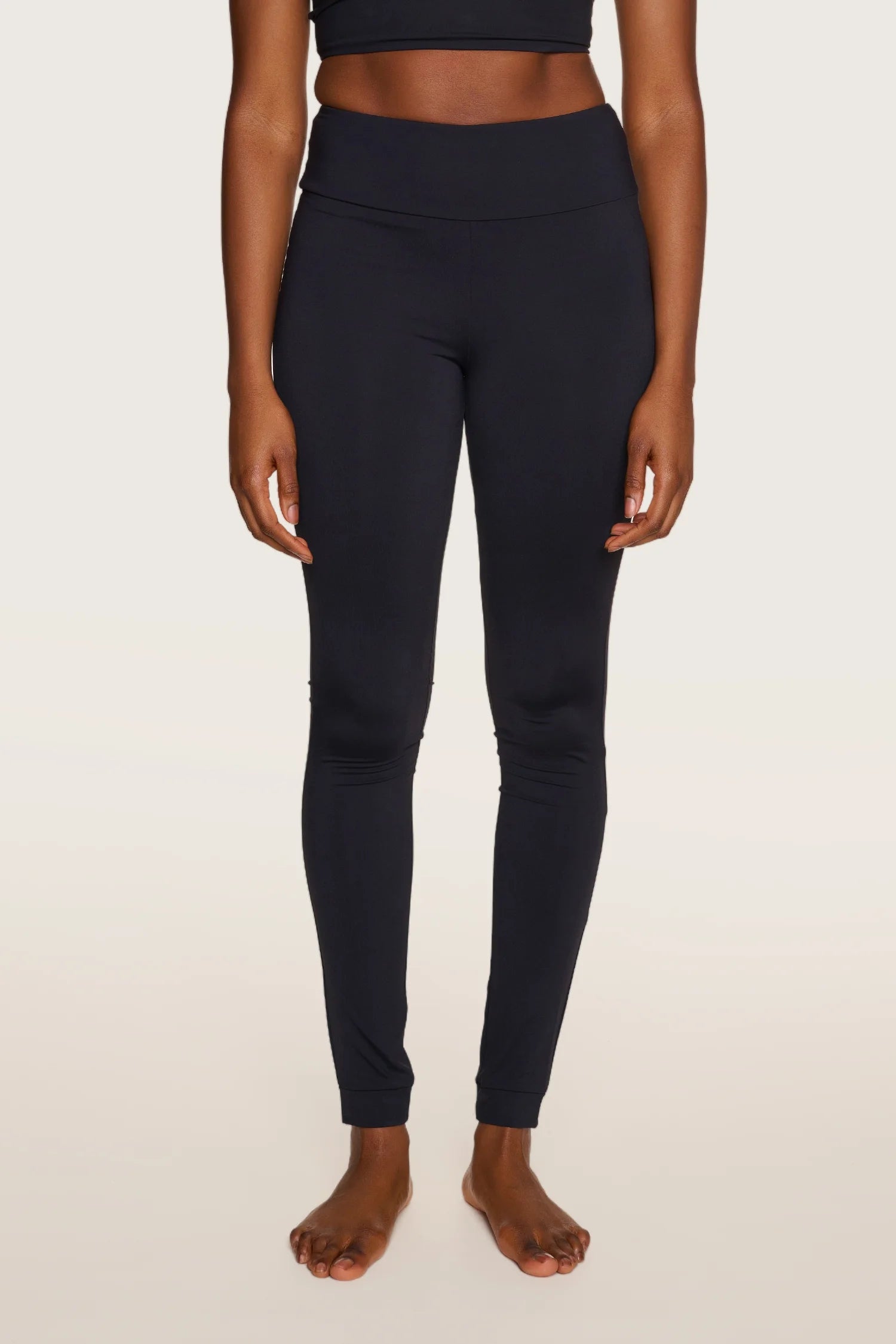 Person trägt schwarze MYMARINI-Leggings mit hohem Bund, stehend vor neutralem Hintergrund.#color_black