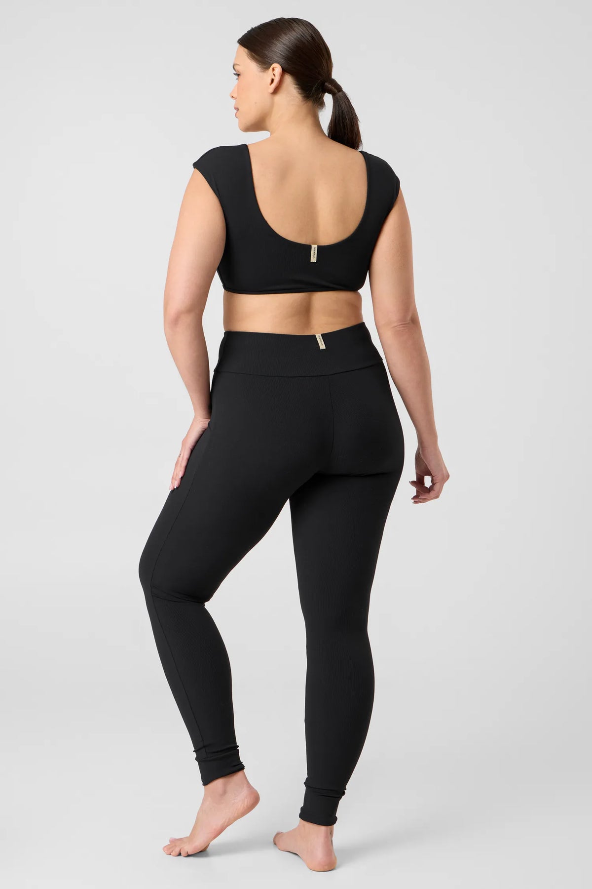 Back view of a woman in the black MYMARINI ALLDAY LEGGINGS with a high waistband and a black bikini top#color_black-ribbed