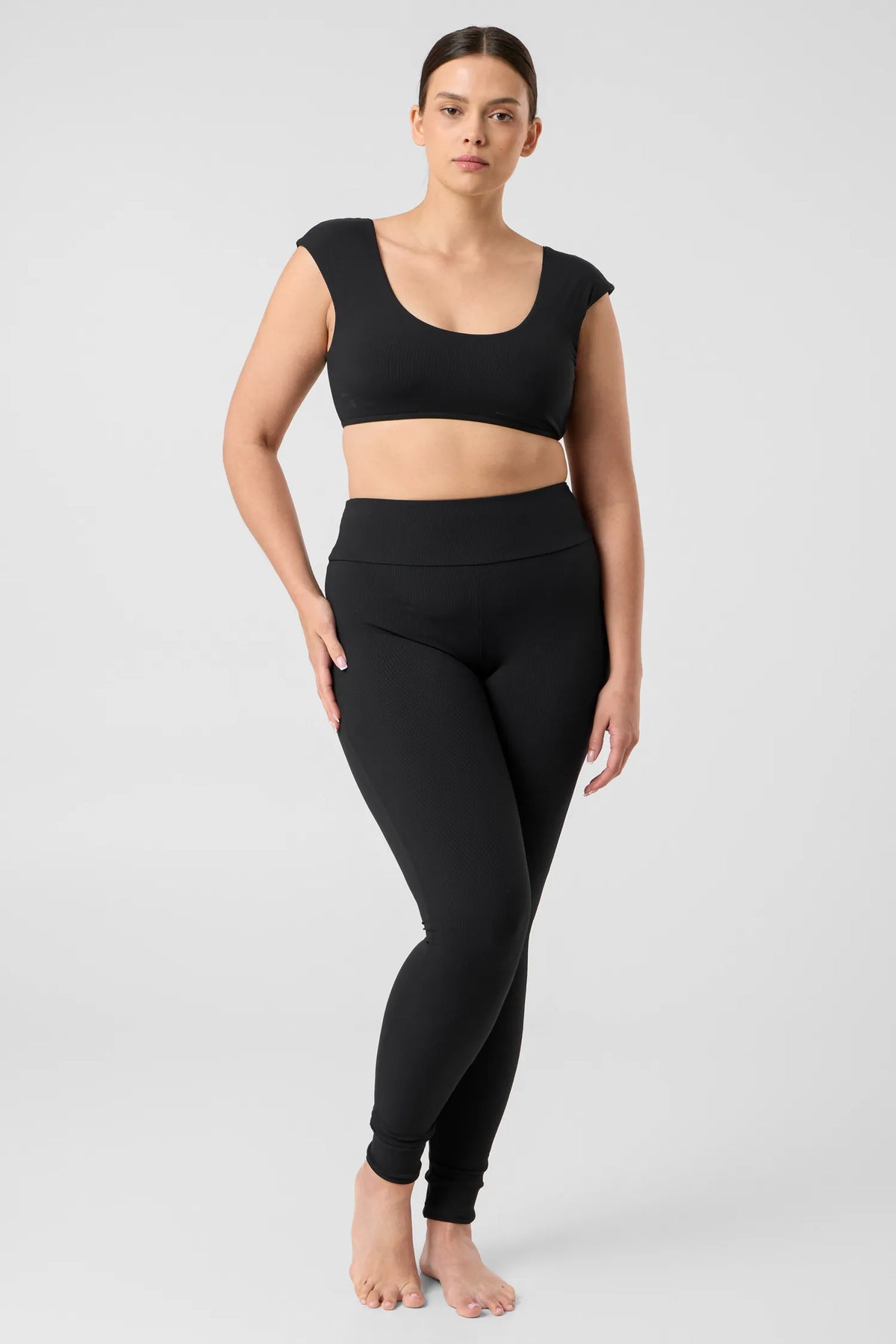 Woman in the black MYMARINI ALLDAY LEGGINGS with a high waistband and a black bikini top, front view#color_black-ribbed