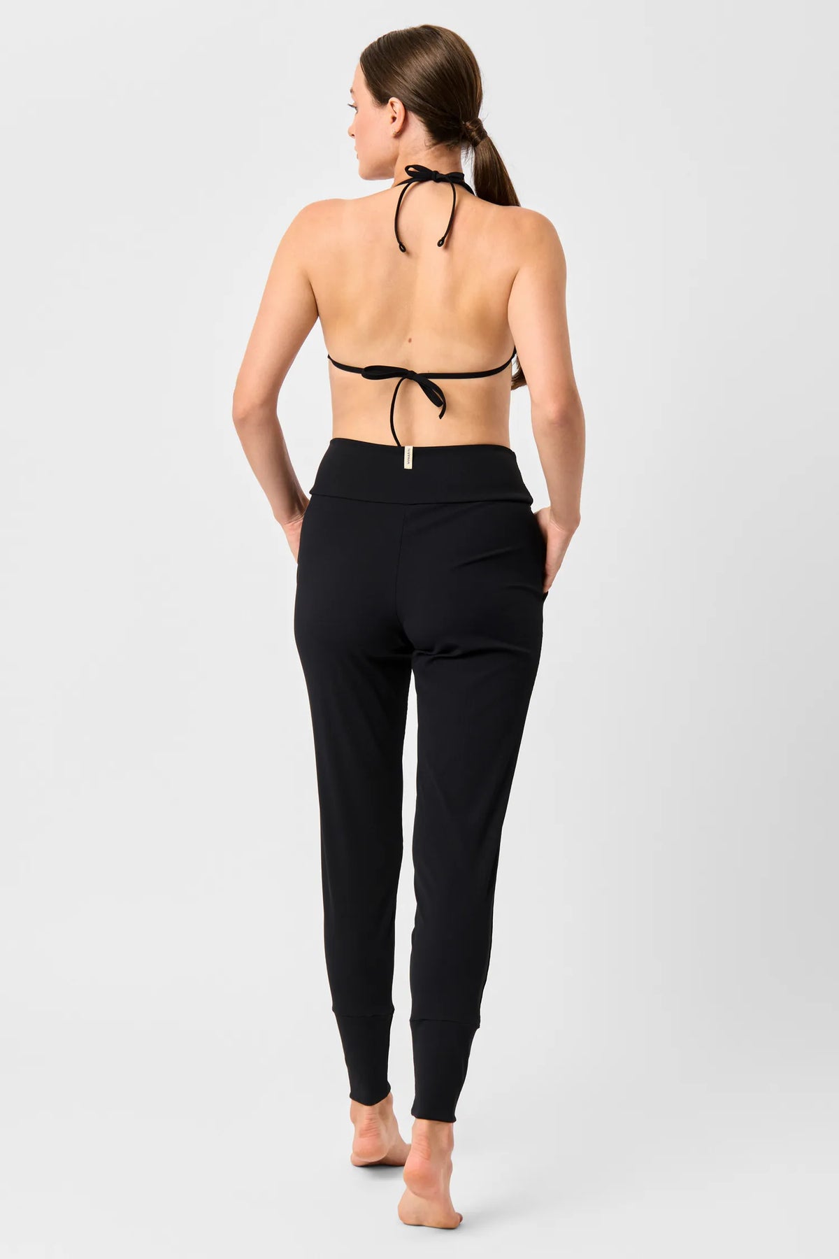 Rückansicht einer Frau in den schwarzen MYMARINI LOOSE LEGGINGS mit schwarzem Neckholder-Bikinitop#color_black-ribbed
