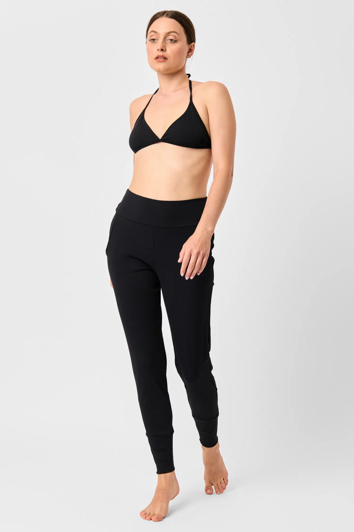 Woman in the black MYMARINI LOOSE LEGGINGS and a black halterneck bikini top, front view#color_black-ribbed