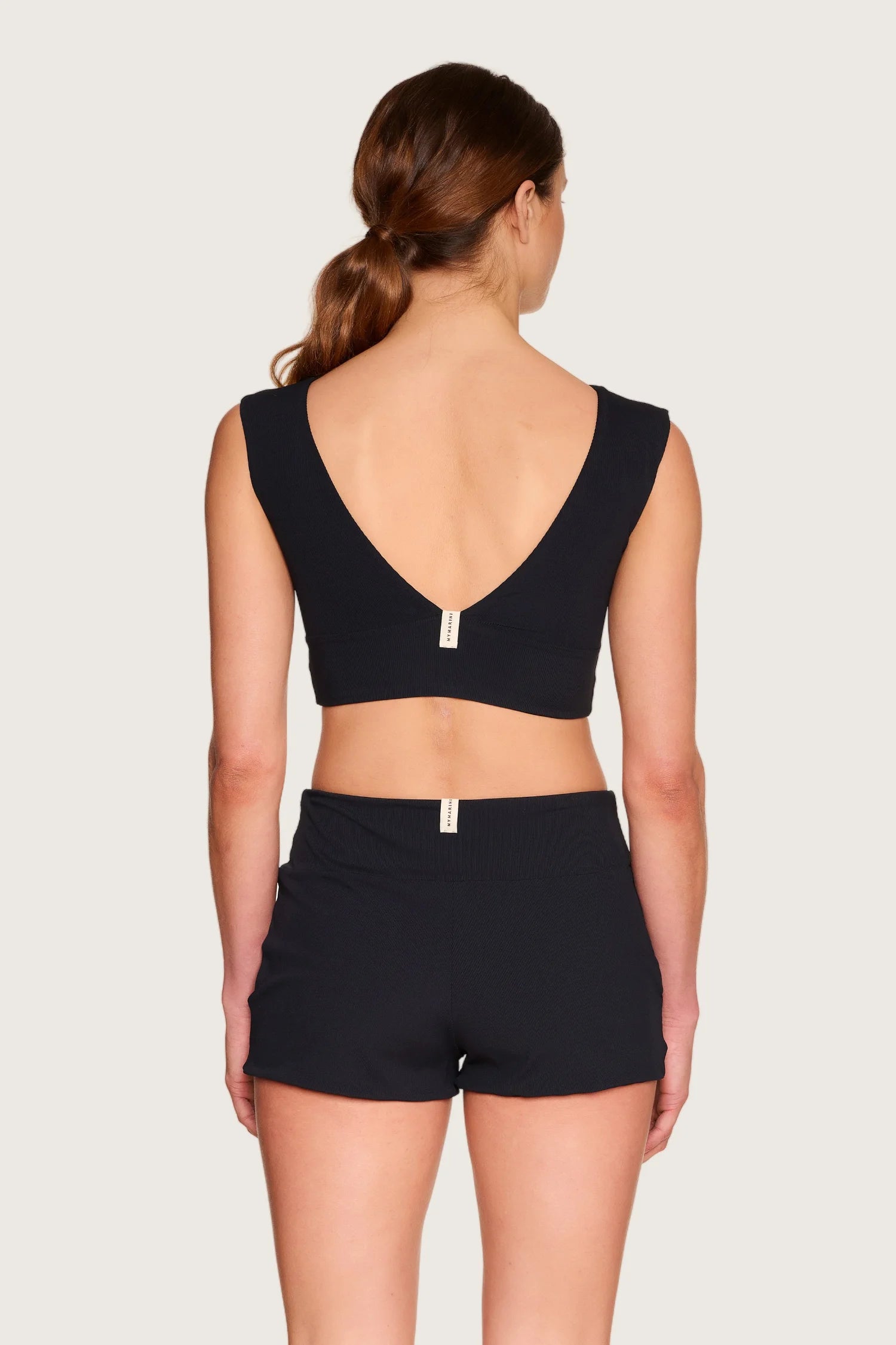 Rückansicht einer Person in schwarzem MYMARINI Bikinitop mit V-Ausschnitt und Shorts.#color_black