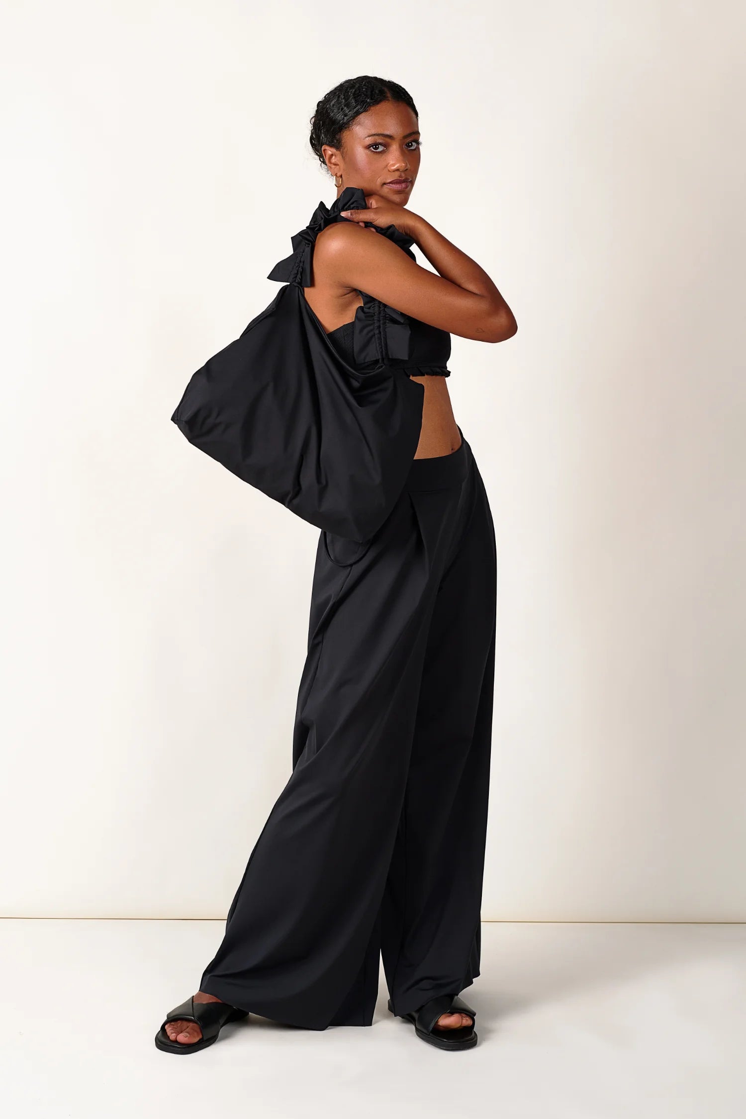 Frau in schwarzem MYMARINI-Top mit breiten Trägern und passender Hose, hält eine große schwarze Tasche.#color_black