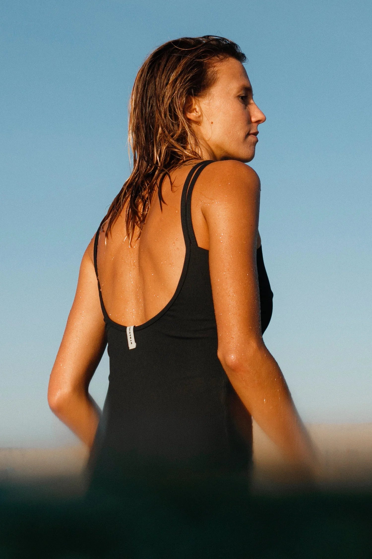 Frau in MYMARINI Badeanzug mit tiefem Rückenausschnitt und breiten Trägern vor blauem Himmel.#color_black