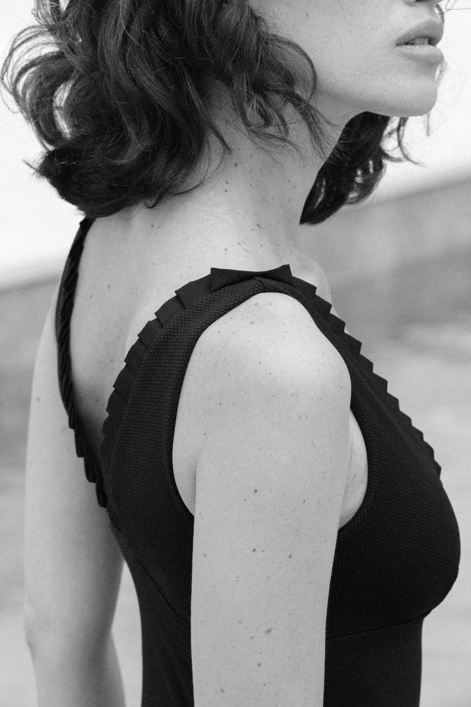 Schwarzer Badeanzug von MYMARINI mit breiten Trägern und Rüschendetails, seitlich abgebildet, vor einem Poolhintergrund.#color_black