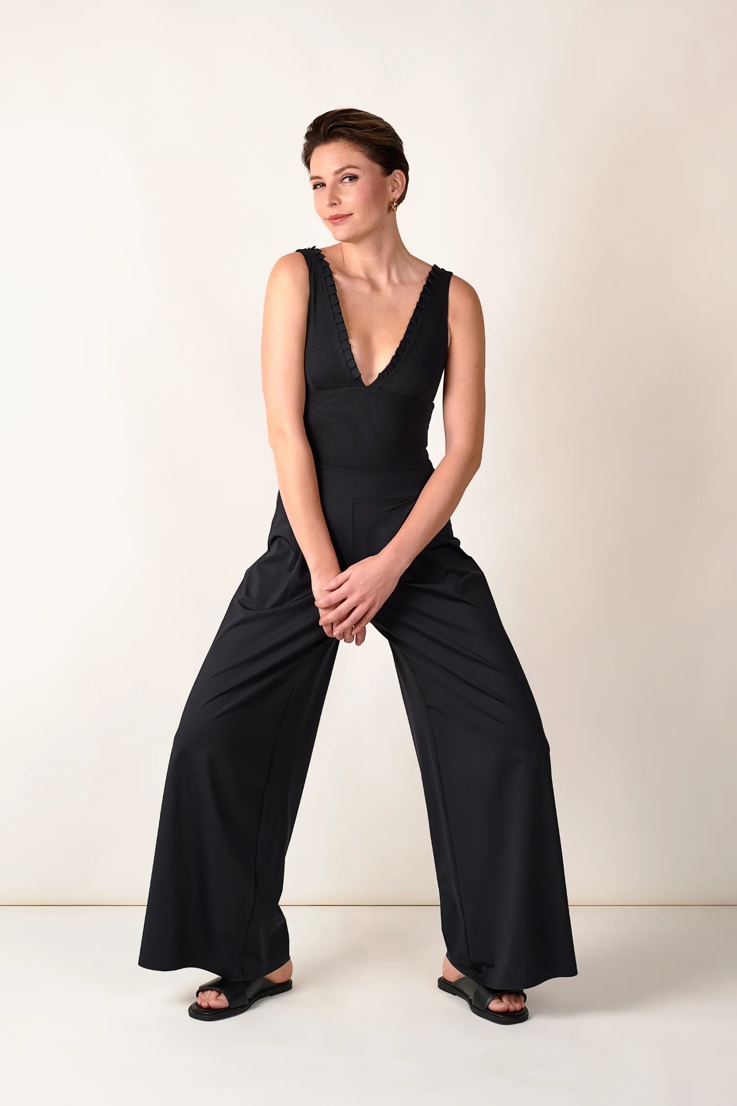 Frau in schwarzem MYMARINI Badeanzug mit V-Ausschnitt und weiter Hose, stehend vor hellem Hintergrund.#color_black