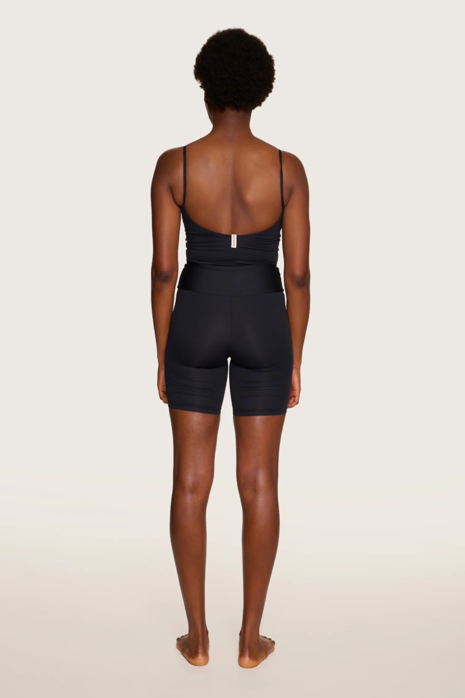 Person von hinten in schwarzem MYMARINI-Badeanzug mit tiefem Rückenausschnitt und Spaghettiträgern vor hellem Hintergrund.#color_black