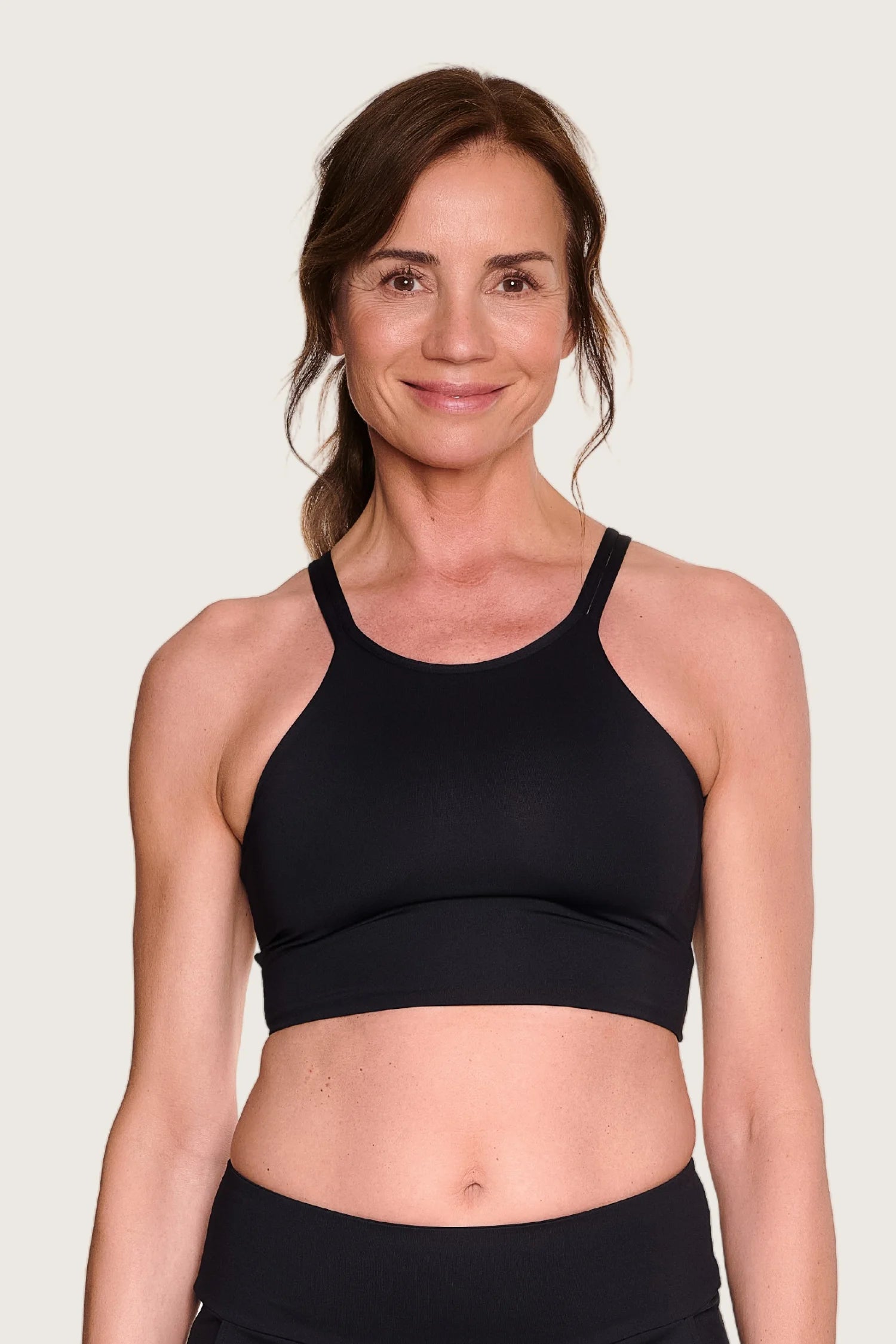 Frau trägt ein schwarzes MYMARINI Bikinitop mit breiten Trägern und hoch geschlossenem Schnitt vor hellem Hintergrund.#color_black