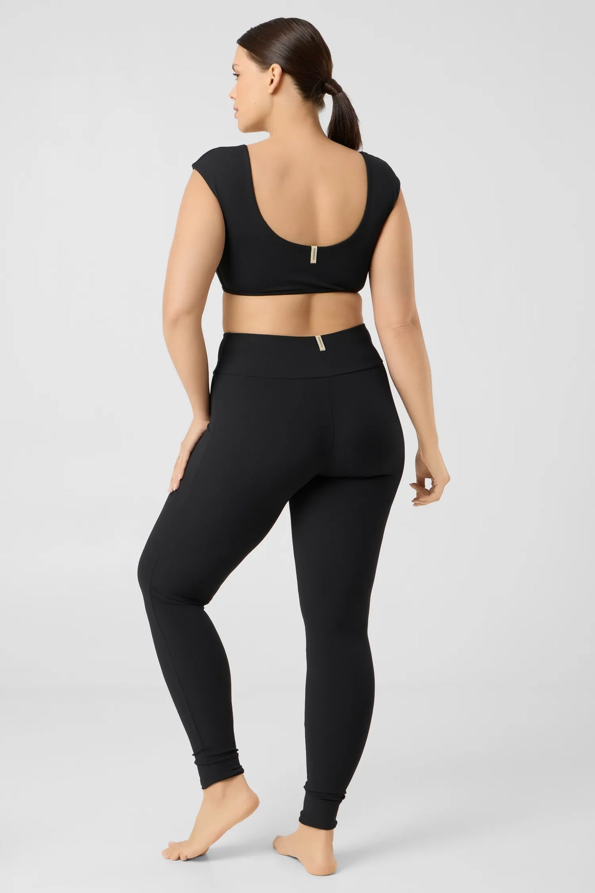 Back view of a woman in the black MYMARINI SHOULDER TOP bikini top with a low back and leggings#color_black-ribbed