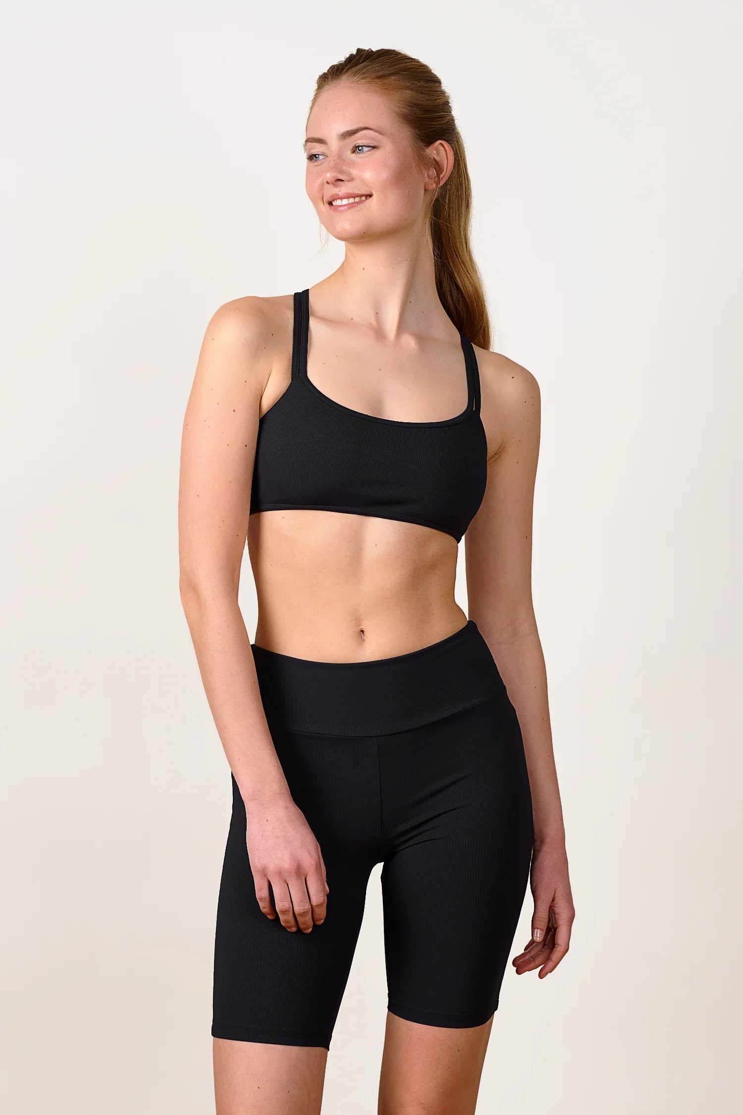 Frau trägt MYMARINI Bikinitop mit breiten Trägern und hoch geschnittene Shorts in Schwarz, lächelnd, vor neutralem Hintergrund.#color_black