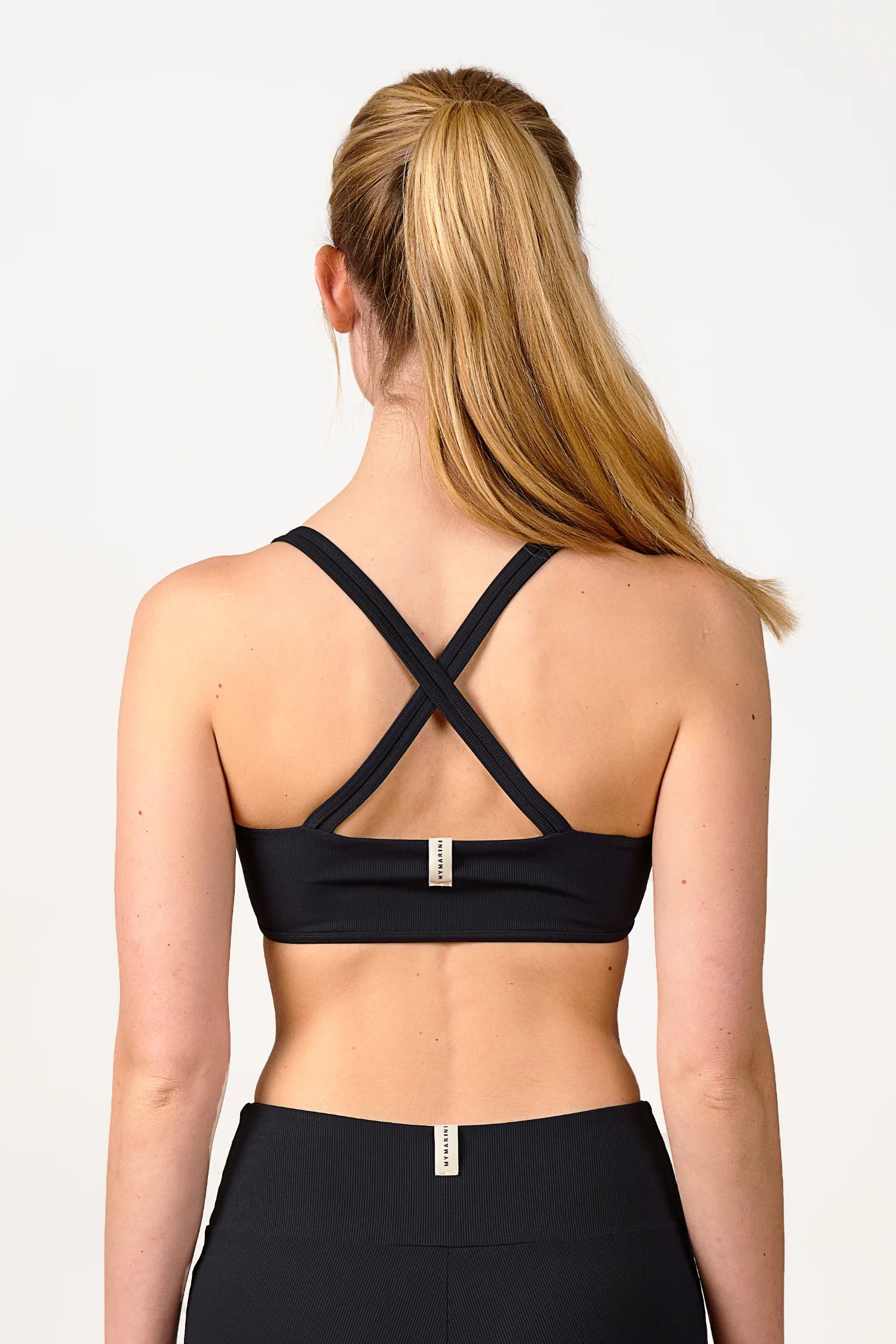 Frau in schwarzem MYMARINI Bikinitop mit Cross-Top-Schnitt, von hinten fotografiert.#color_black