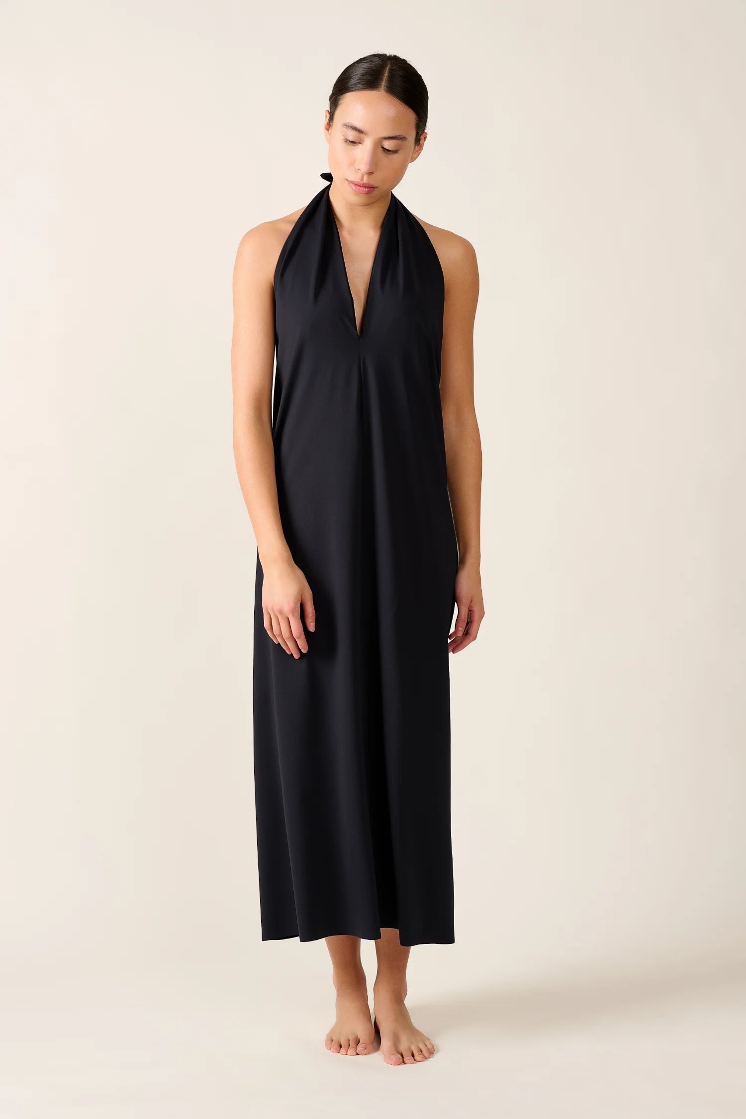 Person trägt ein schwarzes MYMARINI Neckholder-Kleid in knöchellangem Schnitt vor neutralem Hintergrund.#color_black