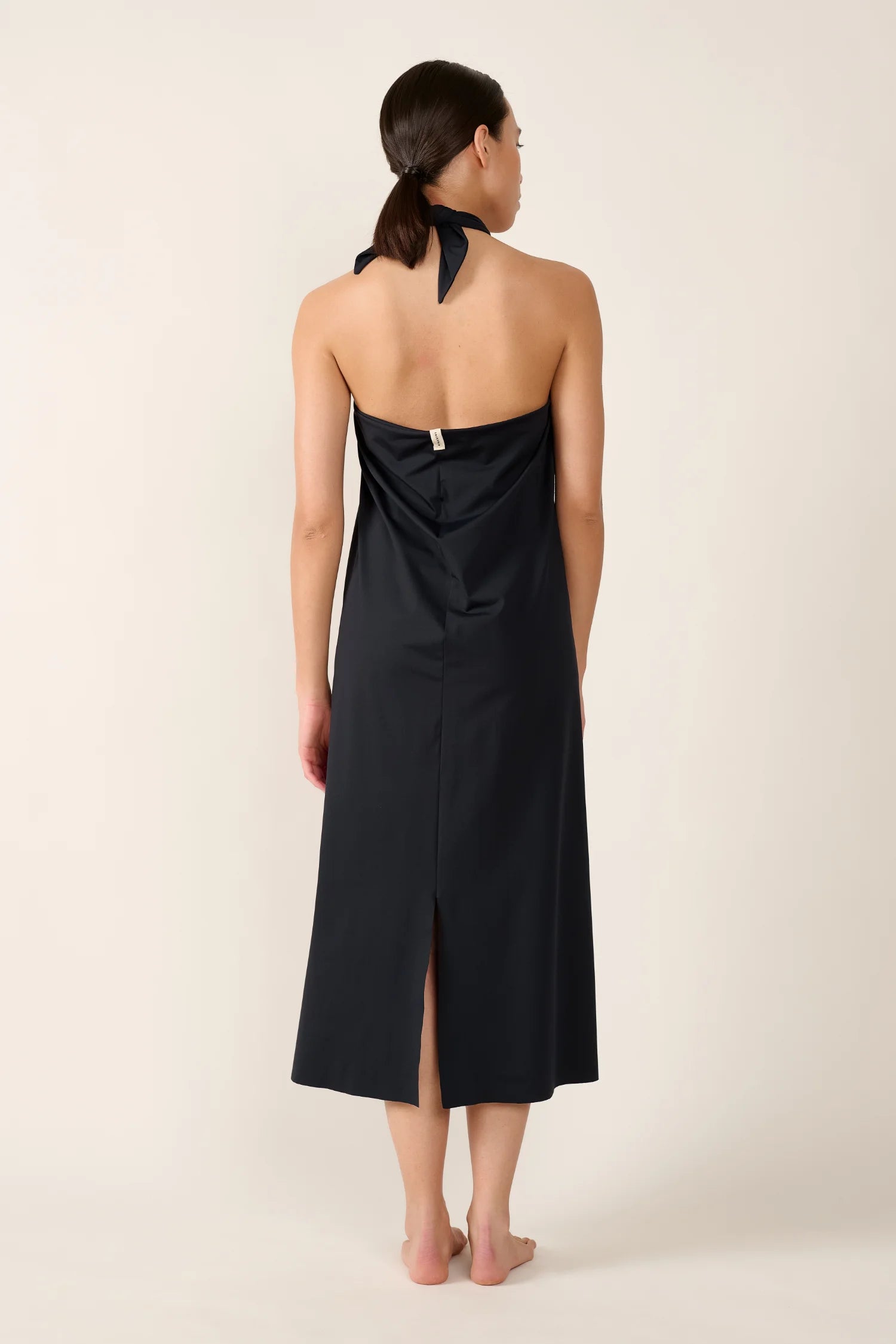 Person von hinten in einem schwarzen MYMARINI Neckholder-Kleid mit mittellangem Schnitt und Rückenschlitz.#color_black
