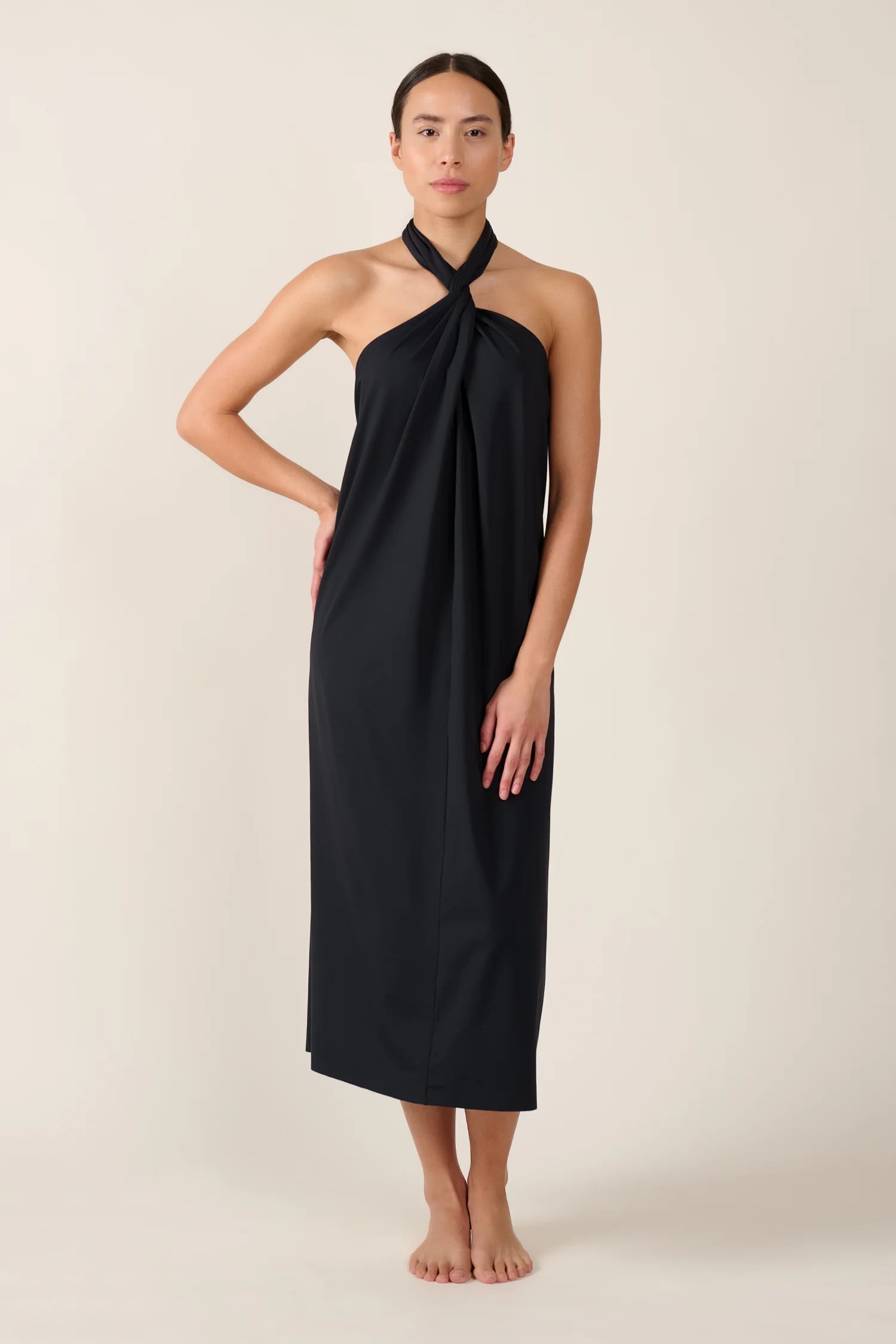 Person trägt ein schwarzes, knielanges Neckholder-Kleid von MYMARINI vor neutralem Hintergrund.#color_black