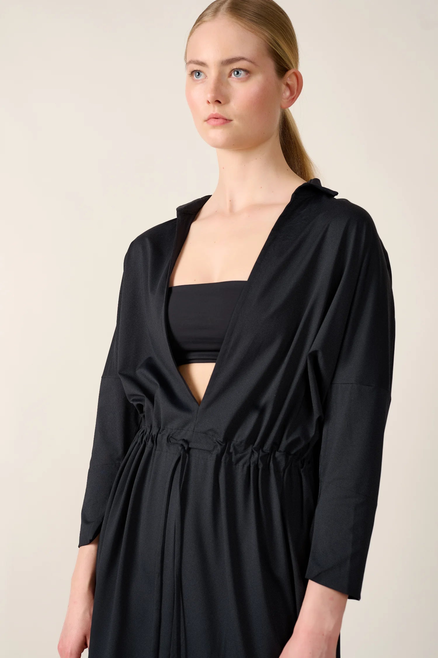Frau trägt schwarzes MYMARINI Bikinitop mit V-Ausschnitt und schwarzem, lockerem Kleid mit Kordelzug in der Taille.#color_black