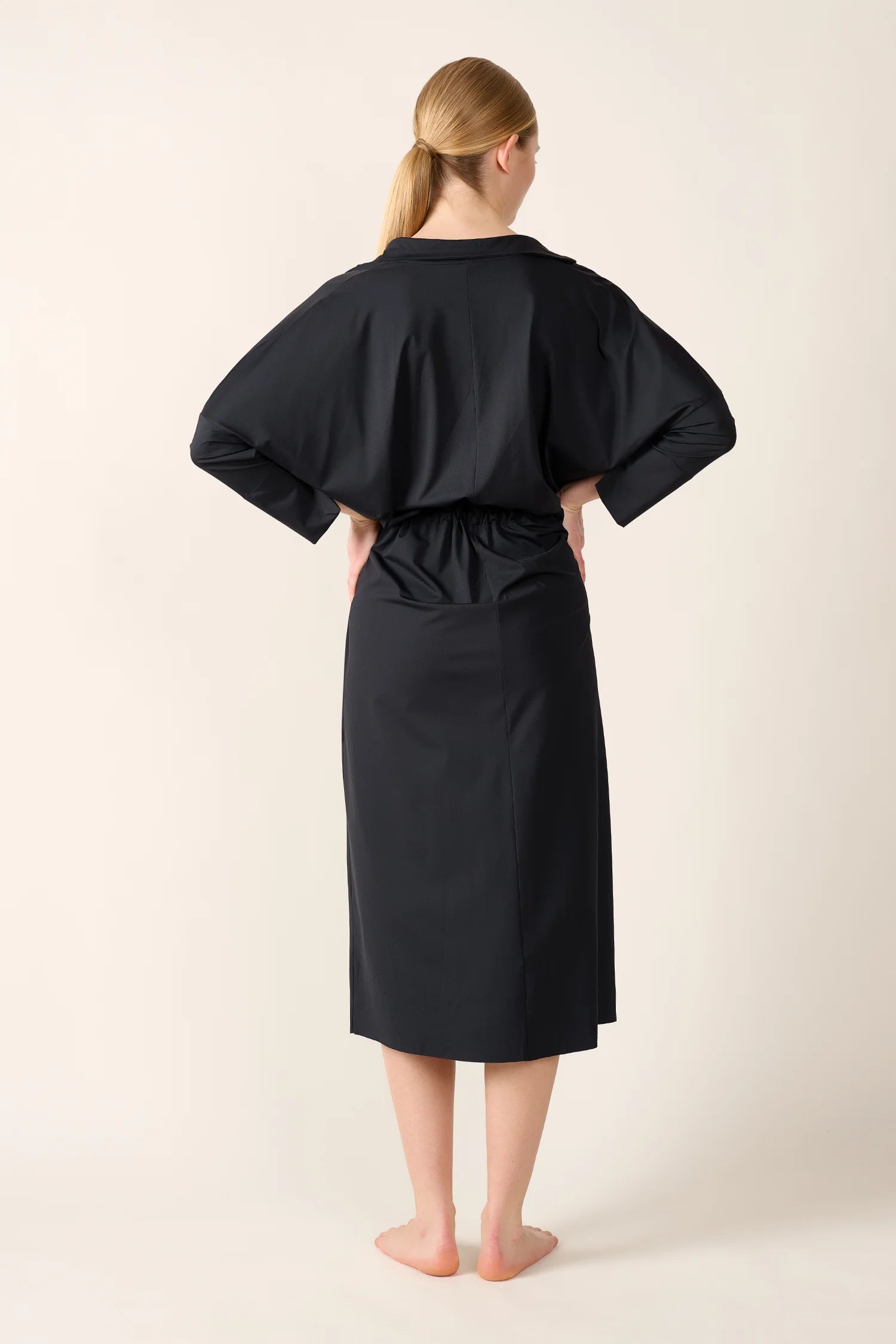 Person von hinten in schwarzem MYMARINI-Kleid mit langen Ärmeln und knielangem Schnitt.#color_black