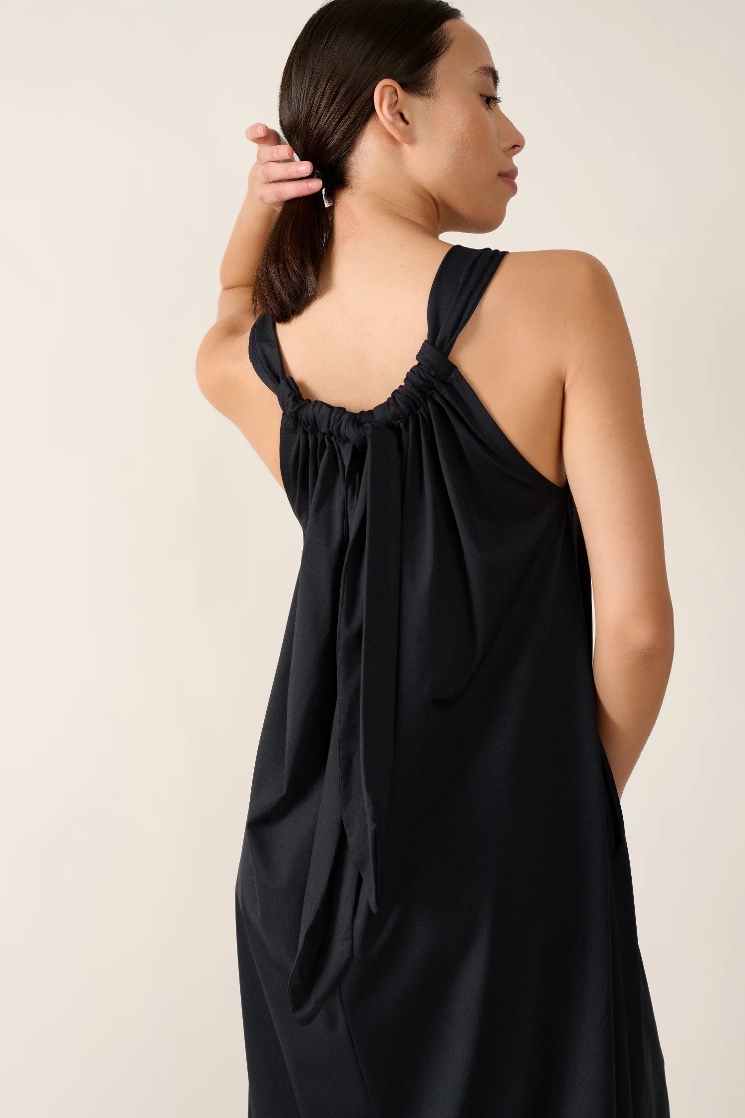 Frau in schwarzem MYMARINI-Kleid mit breiten Trägern, von hinten gezeigt, hält ihr Haar mit der Hand.#color_black