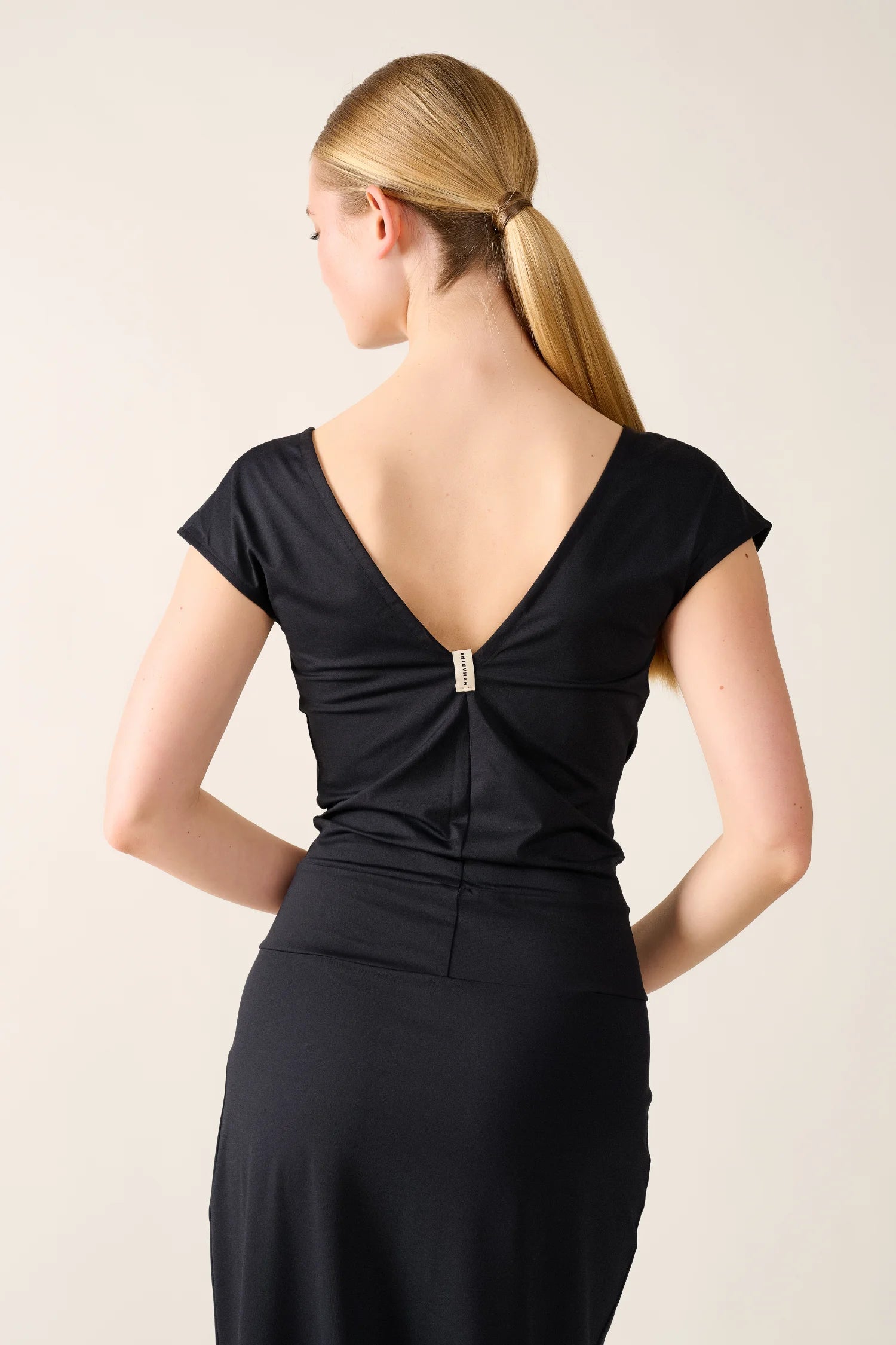 Frau in schwarzem MYMARINI-Kleid mit tiefem Rückenausschnitt, von hinten fotografiert.#color_black