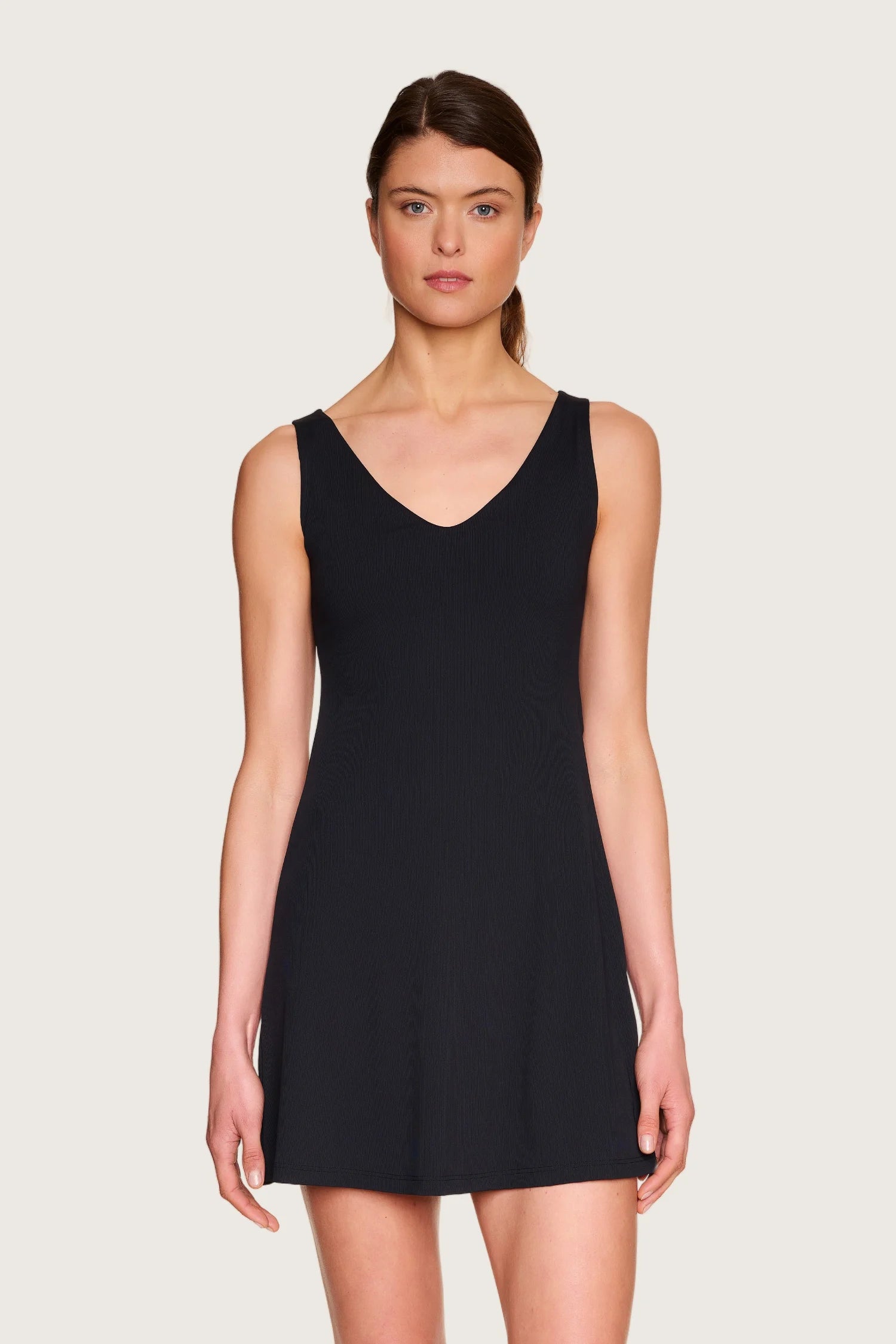 Frau trägt schwarzes MYMARINI-Kleid mit V-Ausschnitt und breiten Trägern vor hellem Hintergrund.#color_black