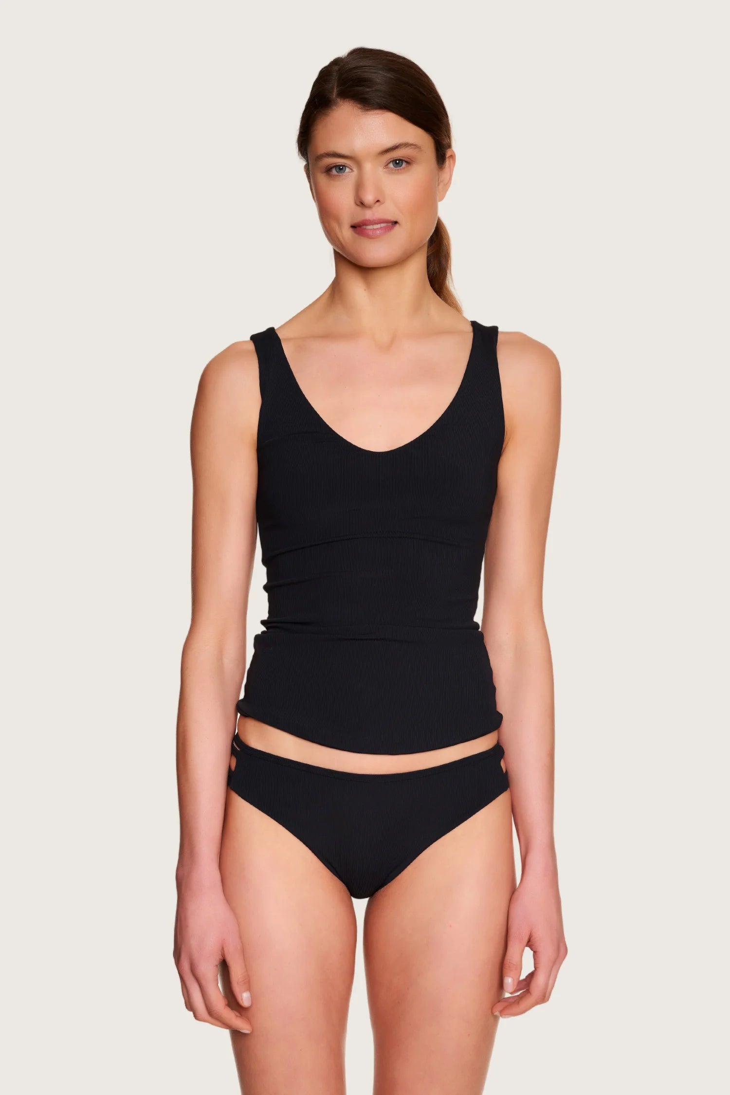 Frau trägt MYMARINI Bikinitop mit V-Ausschnitt und Bikinihose mit Mid rise in Schwarz, vor neutralem Hintergrund.#color_black