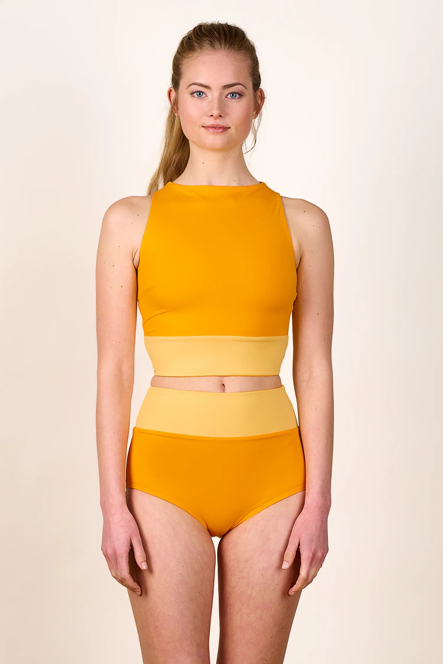 Frau trägt MYMARINI Bikini mit hochgeschlossenem Top und High-Waist-Hose in Gelb.#color_buttermilk-soleil