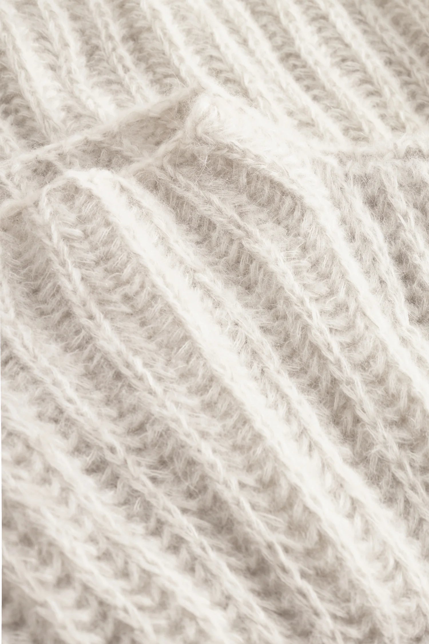 Strickmuster aus weichem, cremefarbenem Garn in Nahaufnahme, zeigt Textur und Details des Materials.#color_white-stone