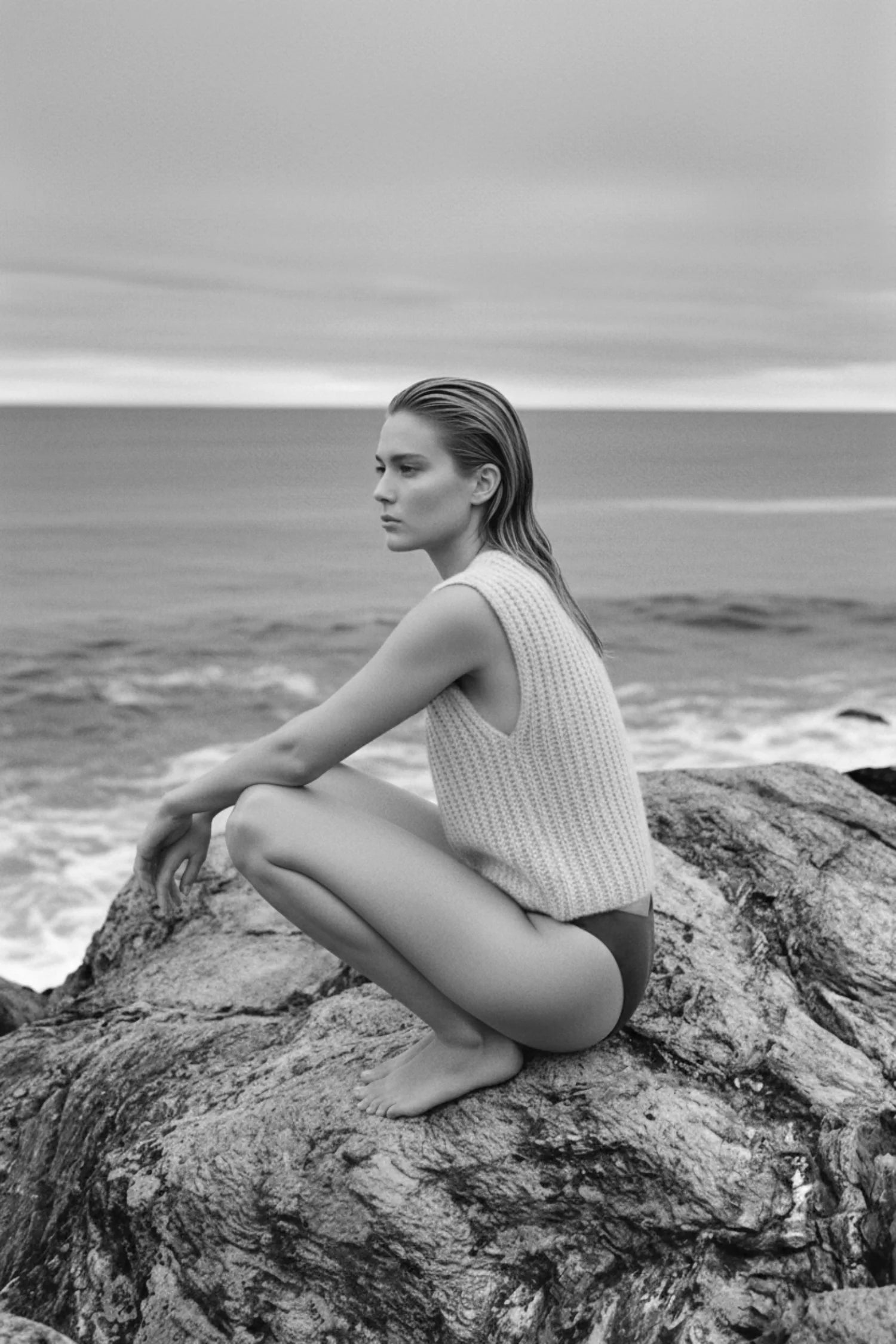 Frau hockt nachdenklich auf Felsen und blickt auf das ruhige Meer hinaus.