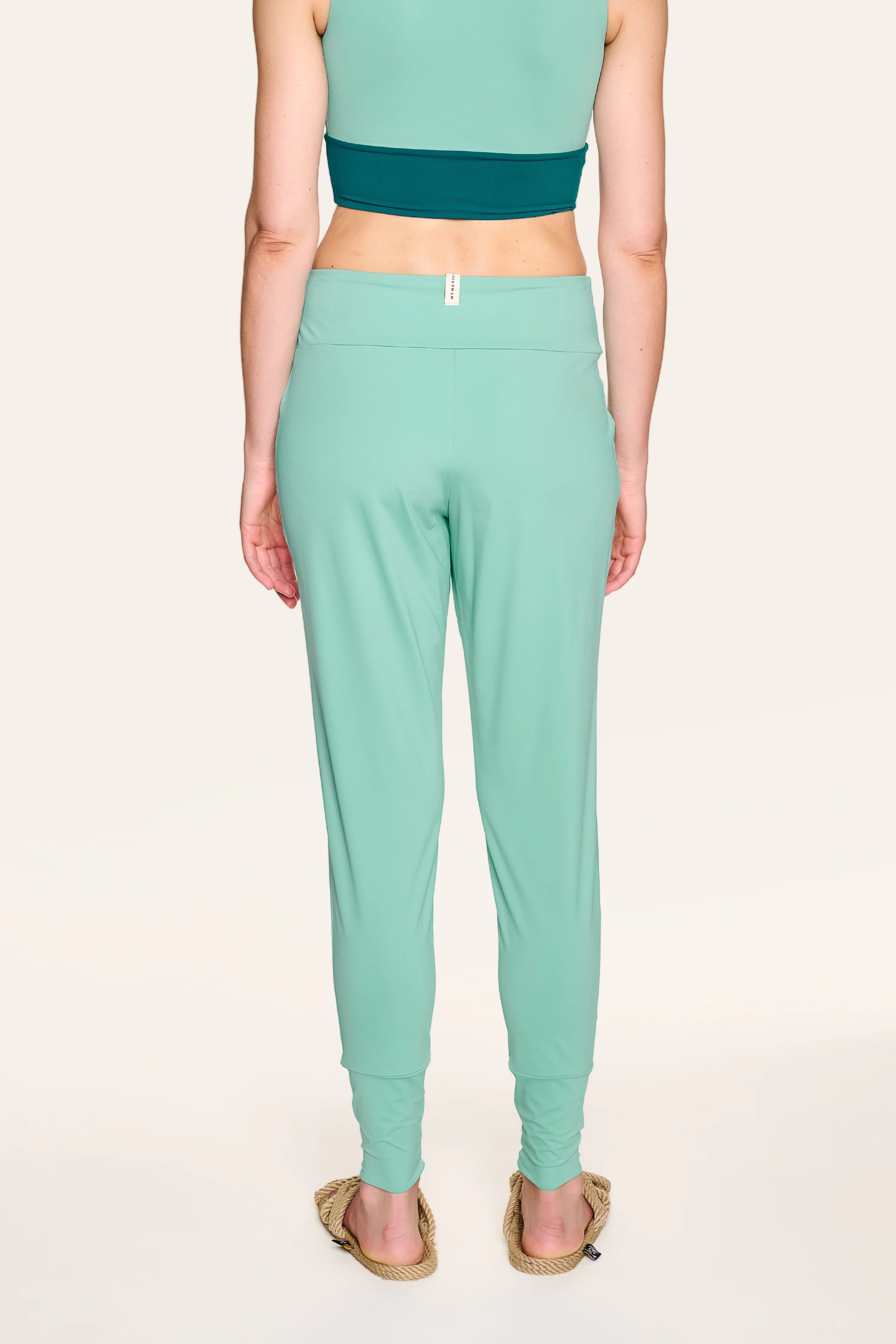 Person von hinten in MYMARINI-Hose in Mintgrün, kombiniert mit einem dunkelgrünen Top.#color_eucalyptus
