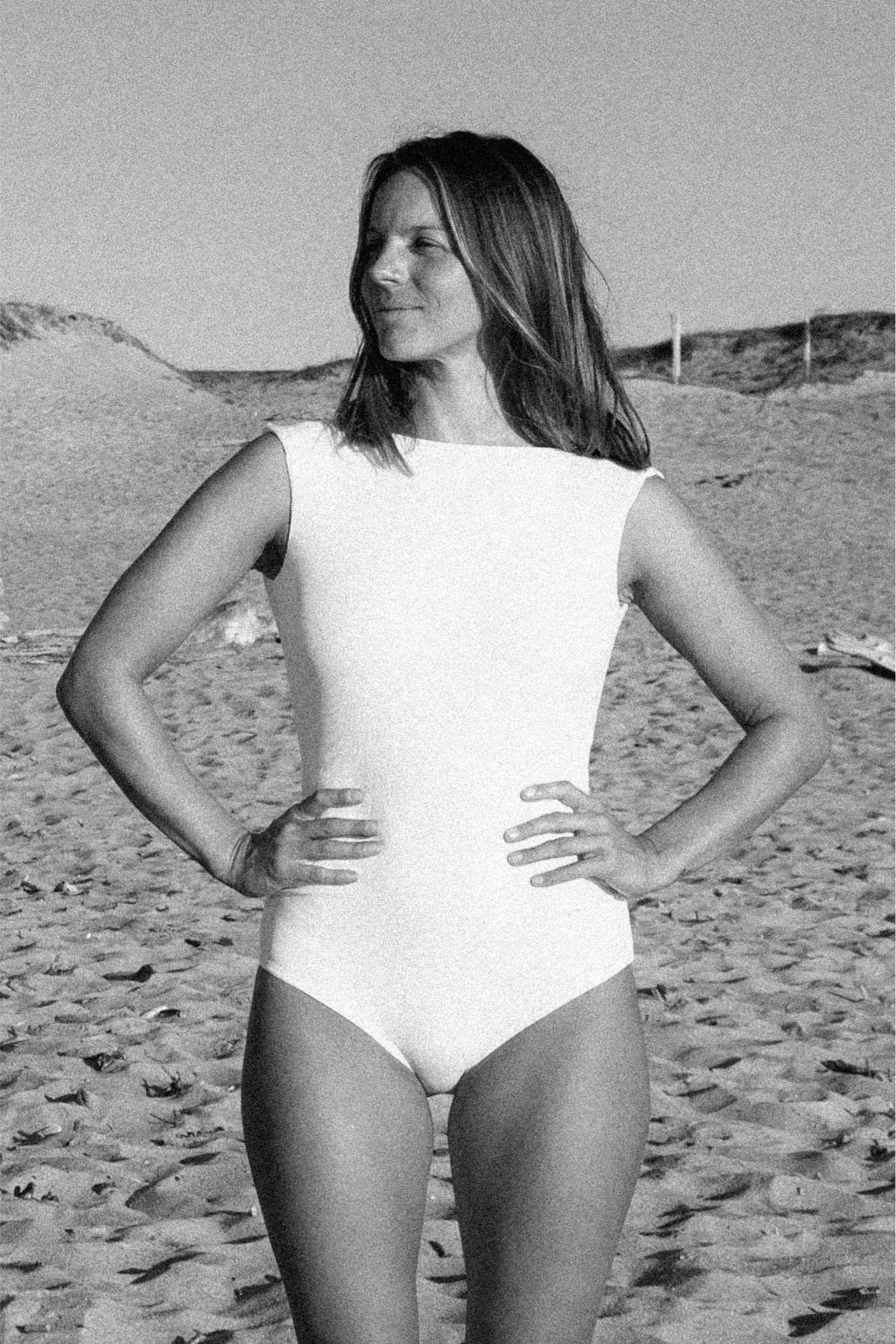 Frau am Strand in MYMARINI Badeanzug mit hochgeschlossenem Schnitt und breiten Trägern.#color_white