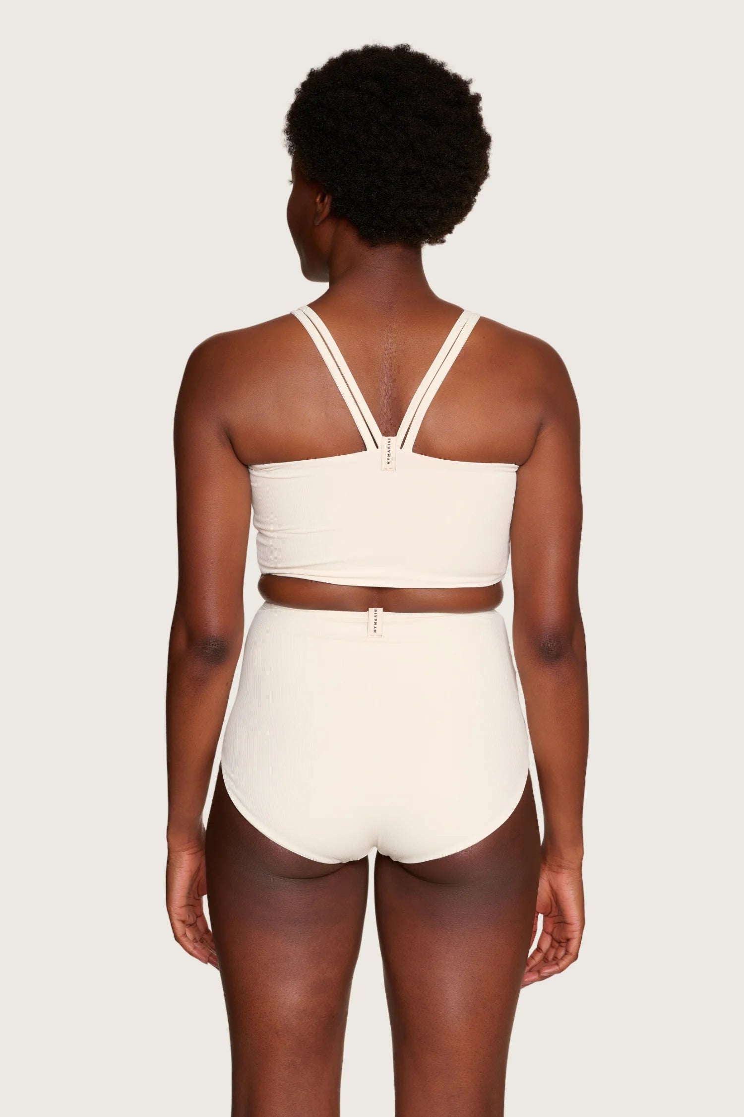 Rückansicht einer Person in MYMARINI Bikinihose und Bikinitop mit breiten Trägern, hoch geschlossen, in Cremeweiß.#color_off-white