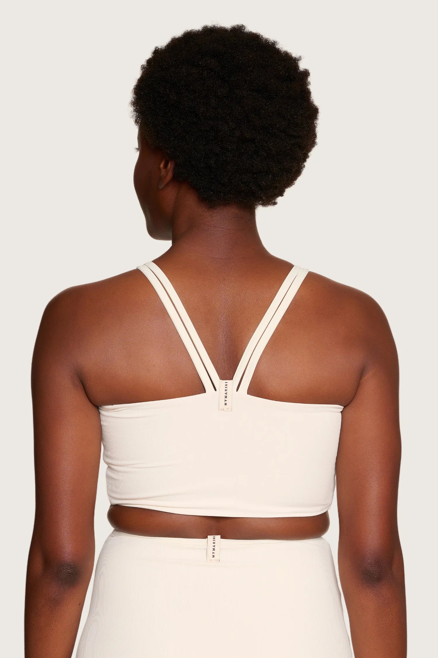 Frau in cremefarbenem MYMARINI-Bikinitop mit breiten Trägern und tiefem Rückenausschnitt, von hinten gezeigt.#color_off-white