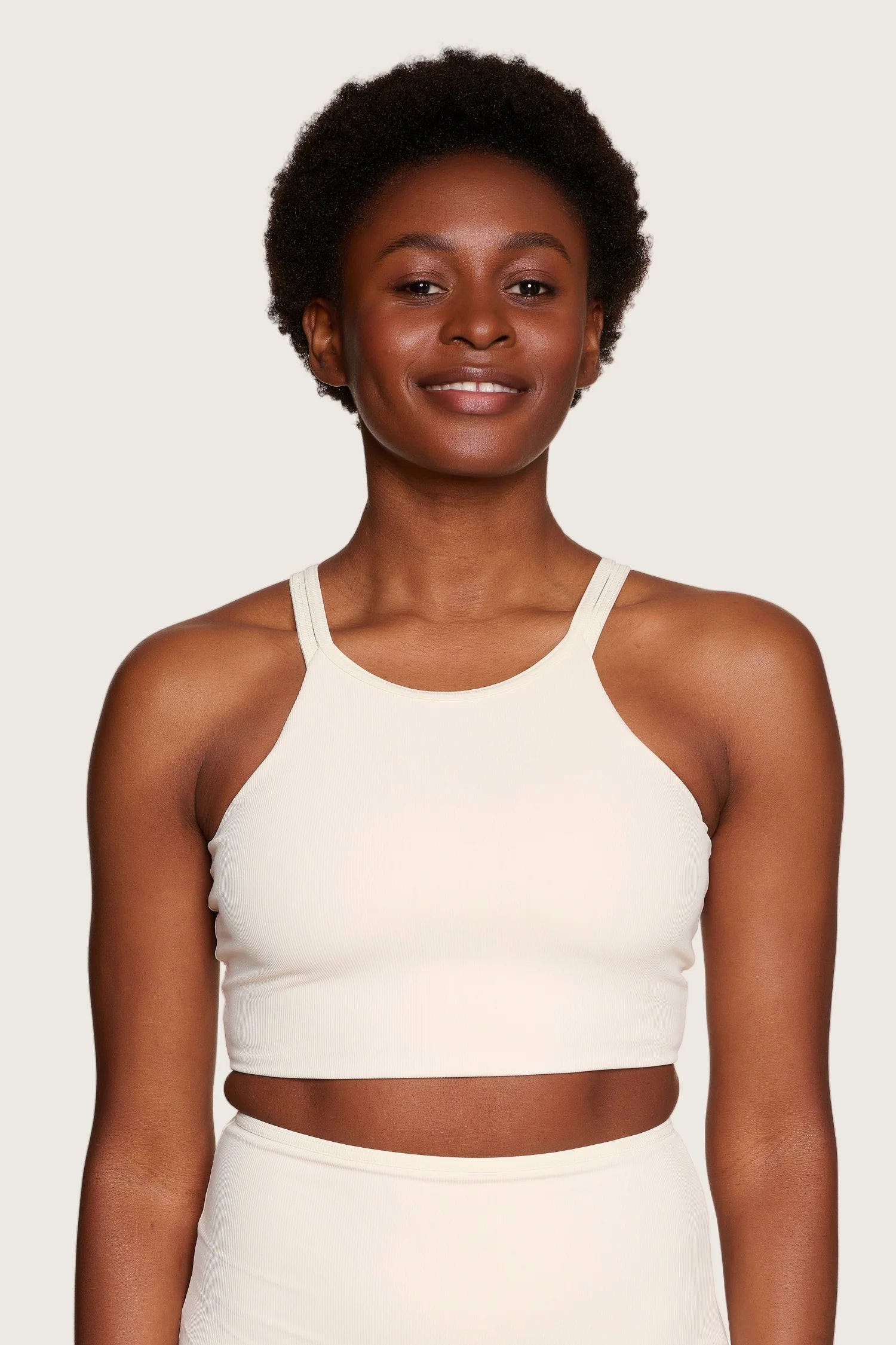 Frau trägt MYMARINI Bikinitop mit breiten Trägern, hoch geschlossen, in hellem Beige vor neutralem Hintergrund.#color_off-white