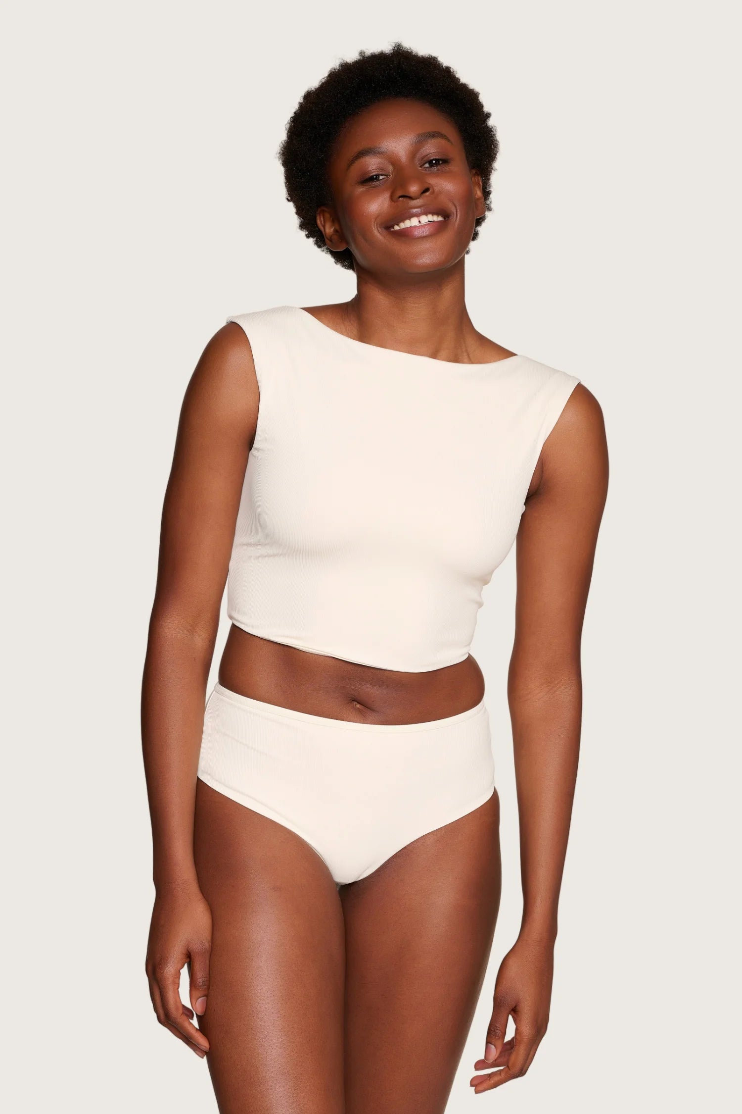 Lächelnde Person trägt MYMARINI Bikinihose mit hohem Beinausschnitt und Top mit breiten Trägern in Cremeweiß.#color_off-white