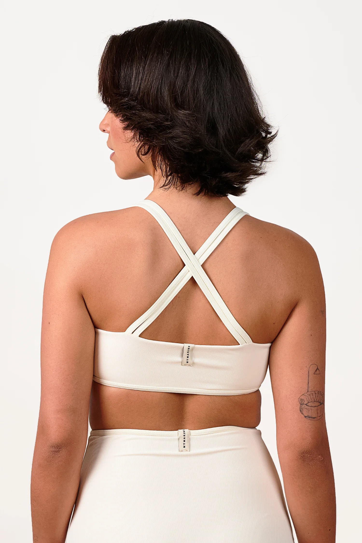 Frau in MYMARINI Bikinitop mit Cross-Back-Trägern und Bikinihose, beide in Cremeweiß, von hinten fotografiert.#color_off-white
