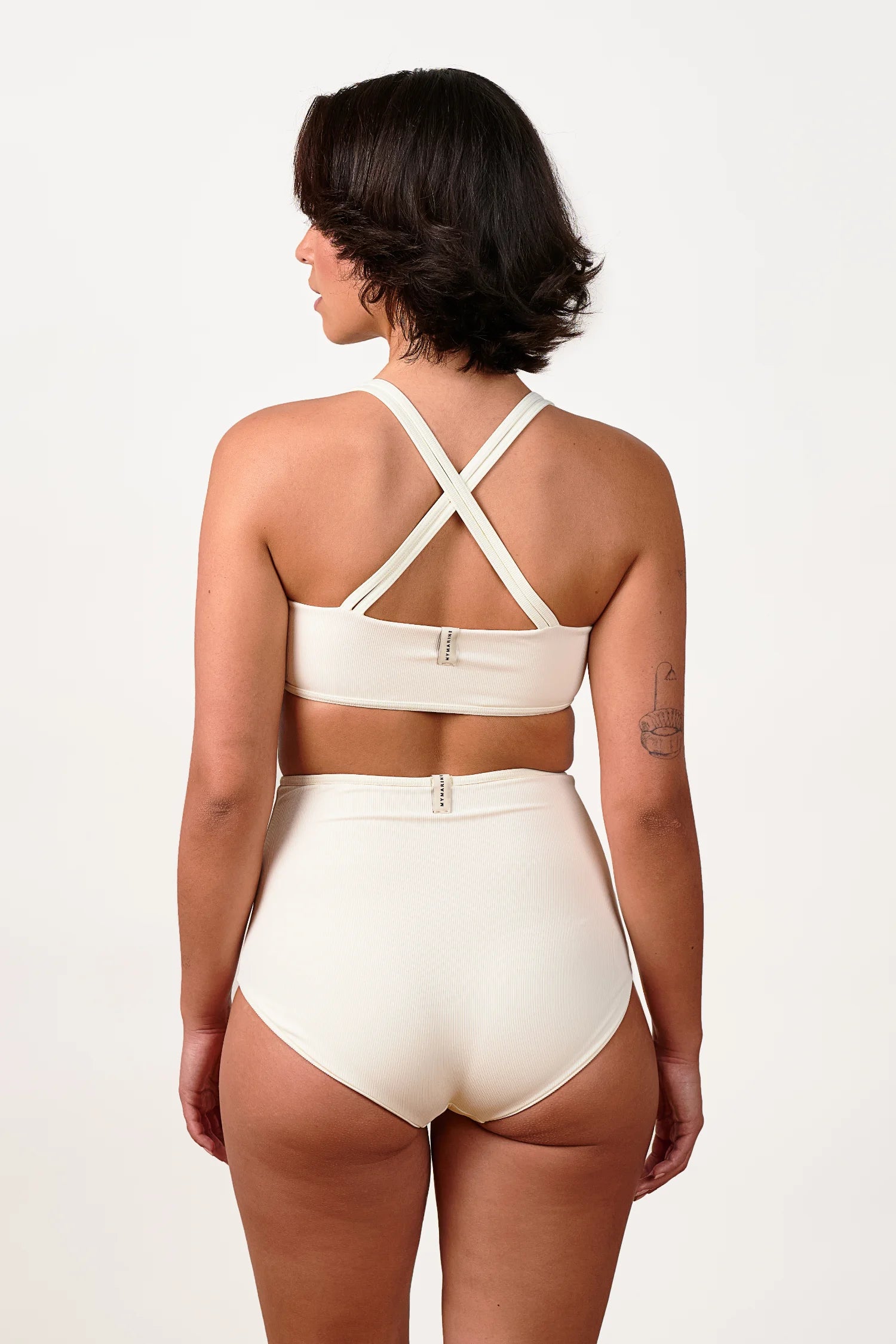 Frau in MYMARINI Bikinitop mit Cross-Back-Trägern und Bikinihose, beide in Cremeweiß, von hinten fotografiert.#color_off-white