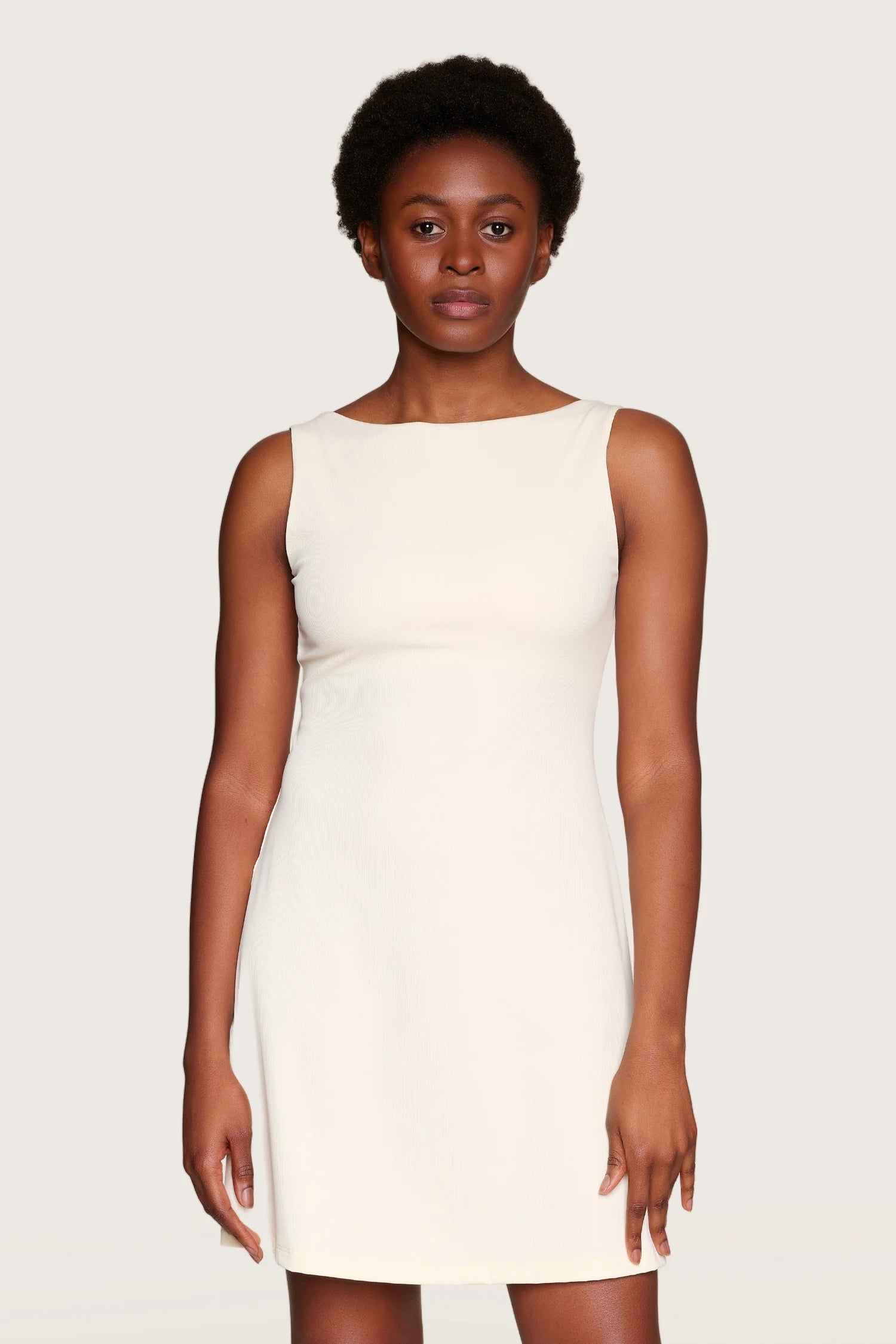 Person trägt ein ärmelloses, cremefarbenes MYMARINI-Kleid mit Rundhalsausschnitt.#color_off-white