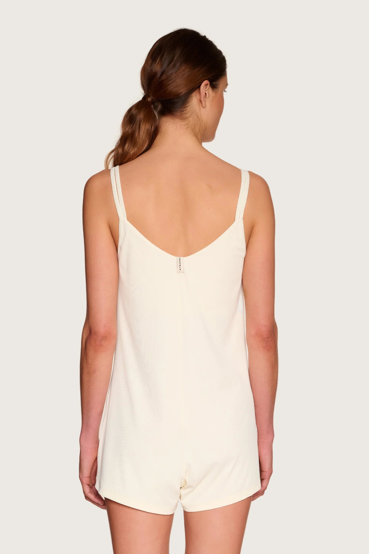 Frau von hinten in cremefarbenem MYMARINI-Overall mit Spaghettiträgern und tiefem Rückenausschnitt.#color_off-white