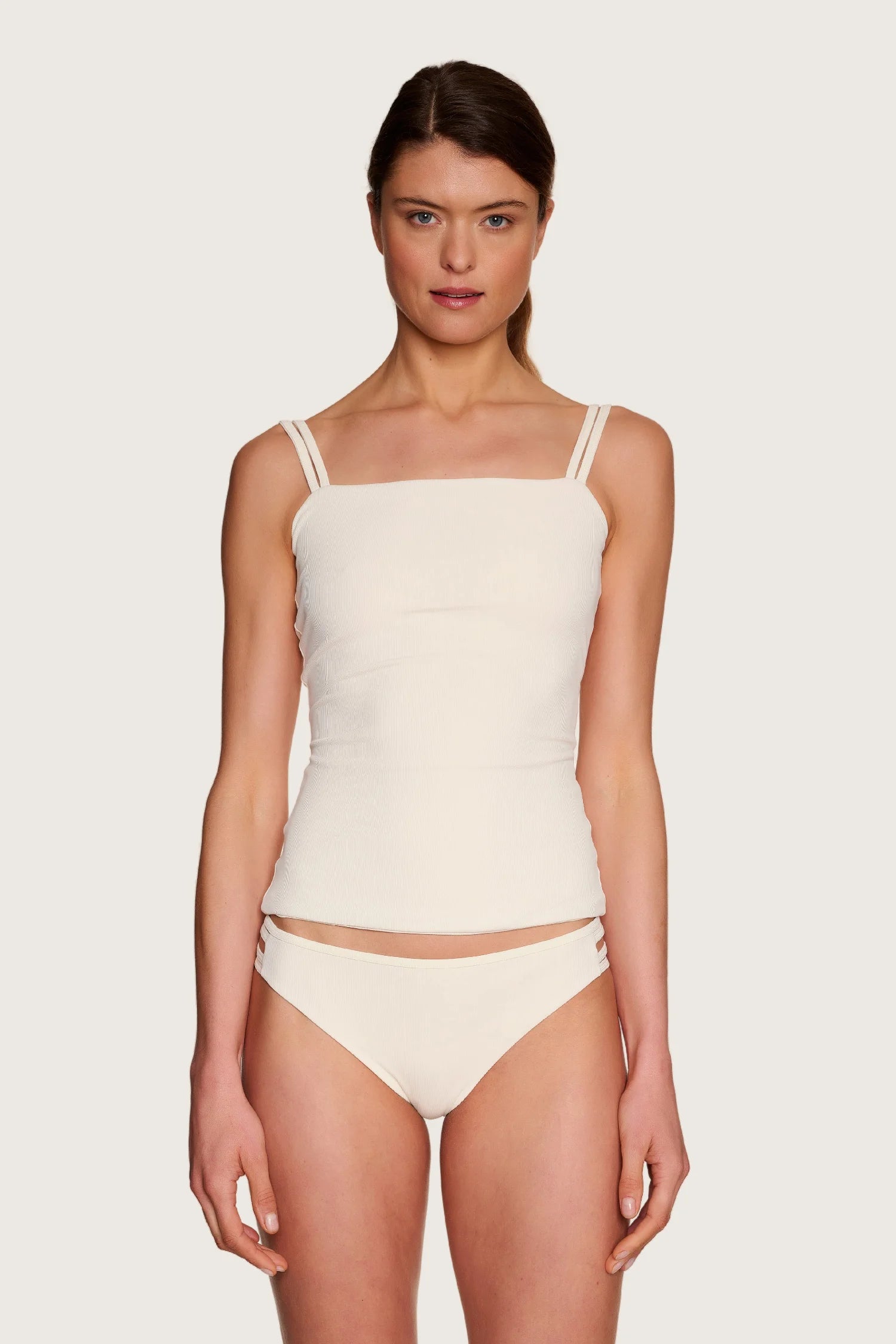 Frau trägt MYMARINI Bikinitop mit geradem Ausschnitt und Spaghettiträgern in Creme, dazu passende Bikinihose.#color_off-white